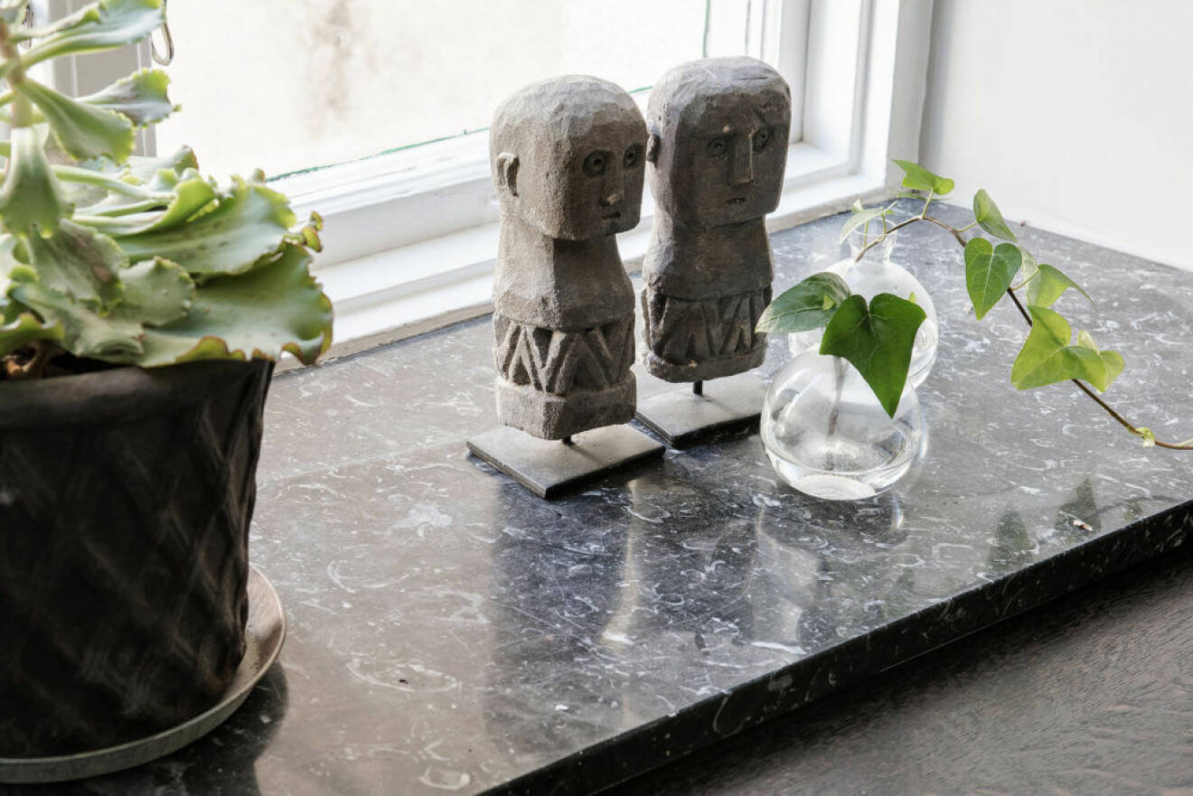 Fönsterbräda där små dekorativa skulpturer står sida vid sida med krukväxter och små minivaser