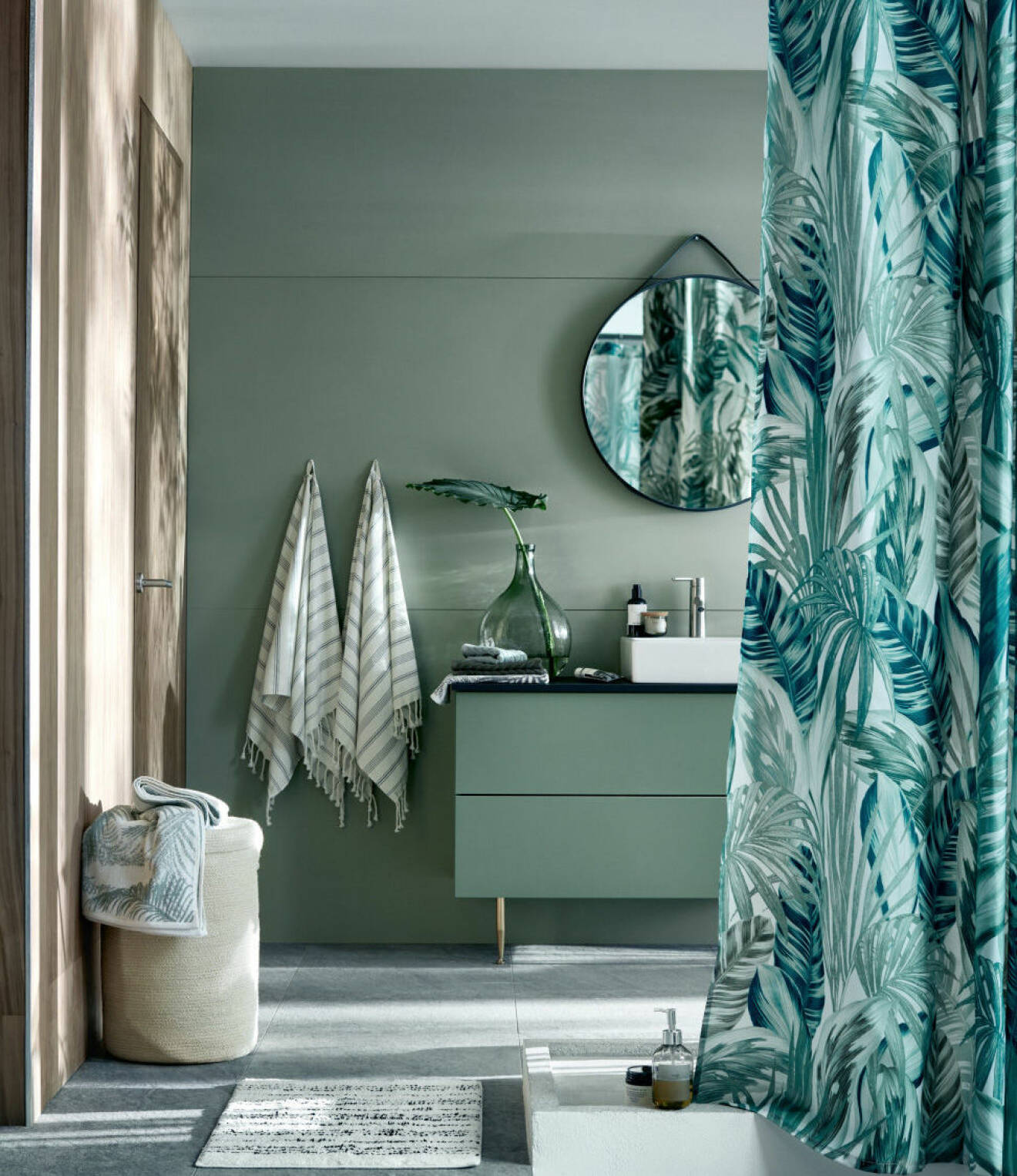 Badrum i grönt, grönt duschdraperi och rund spegel. 