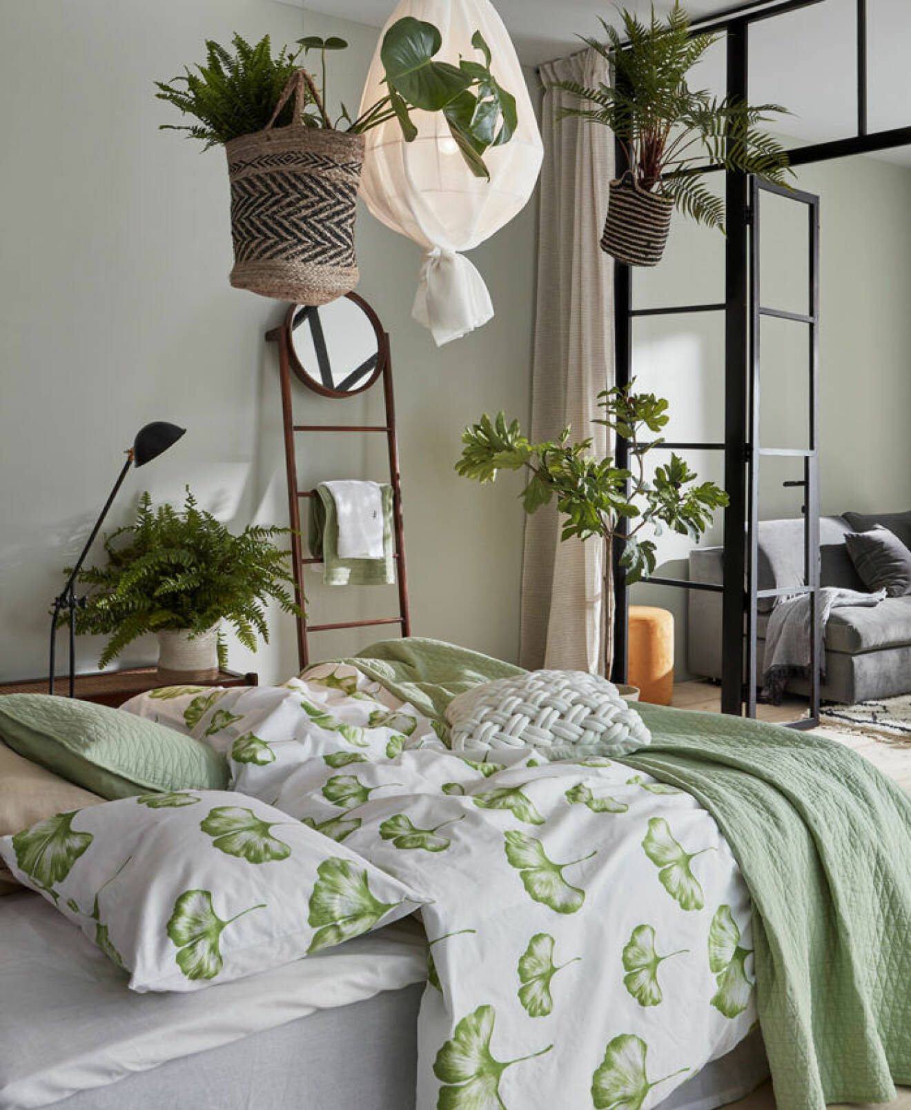 Sovrum med gröna sängkläder och amplar med gröna växter. Glasvägg i industristil. Jotex vår och sommar 2018. 