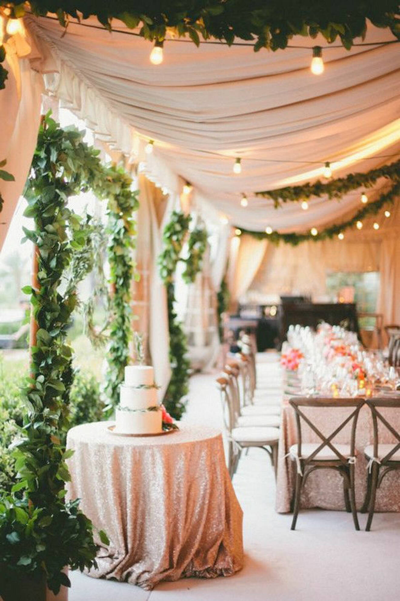Bröllopsmiddag, bröllopslokal med rosa tyger, ljusslingor och gröna växter som dekoration.