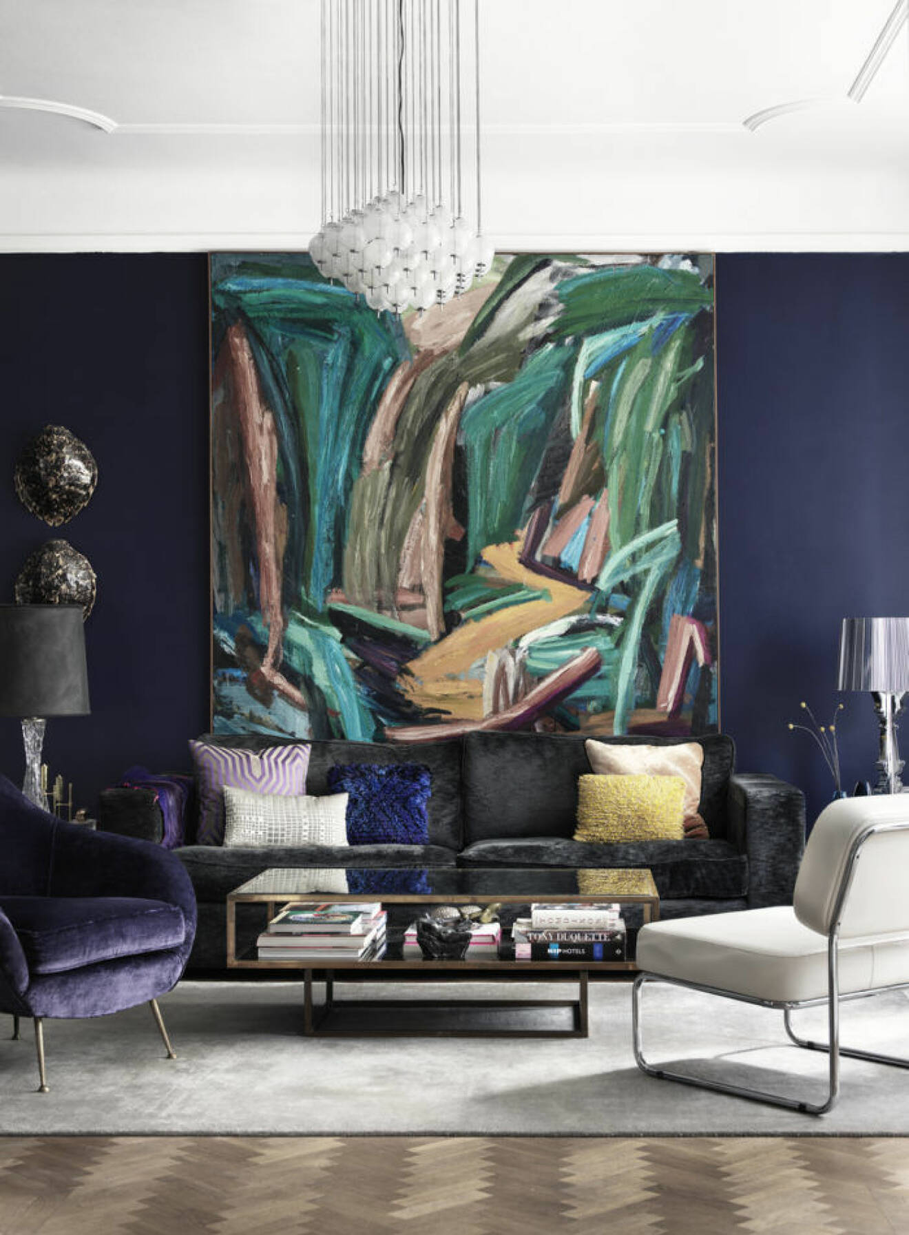 Stor abstrakt tavla i vardagsrum med färgglada sammetskuddar i mörkgrå sammetssoffa.