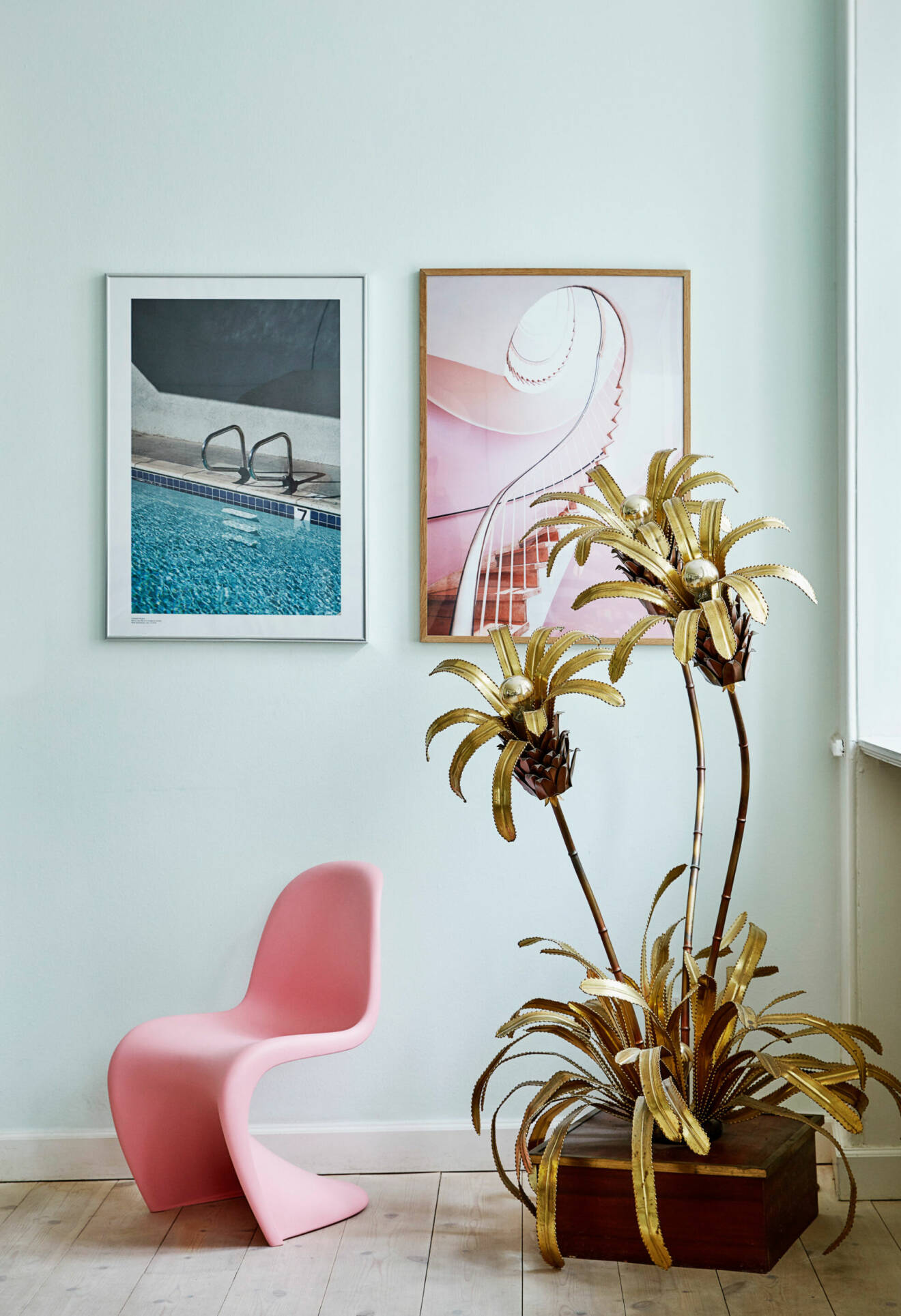 Rosa stol, palmdekoration och två tavlor i ett fint stilleben