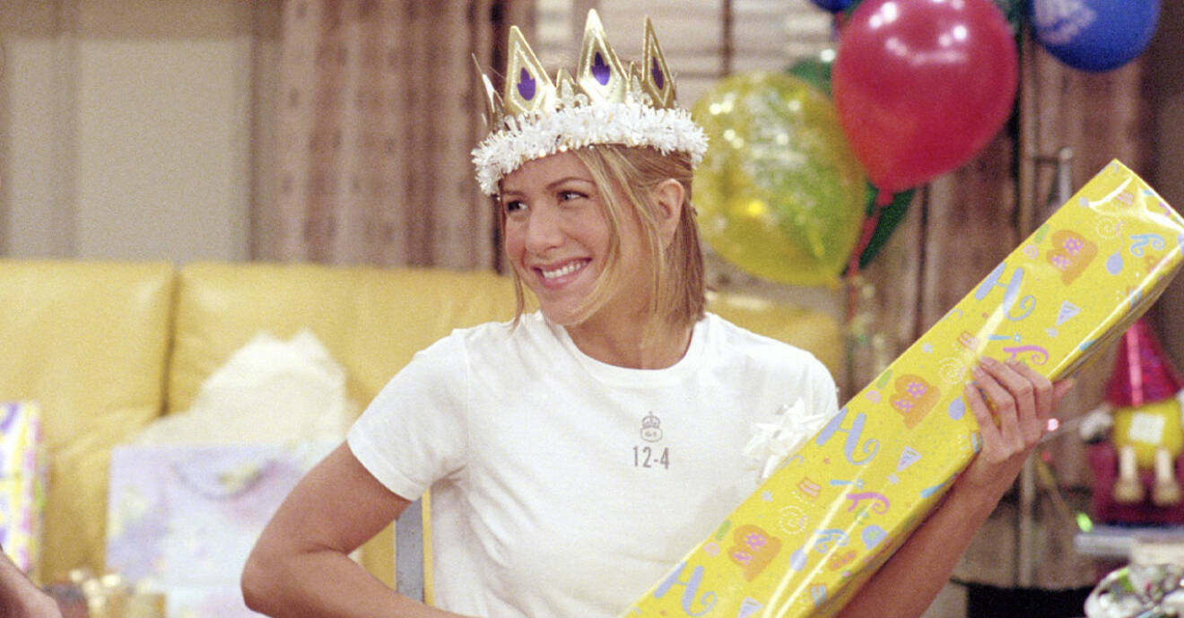 Jennifer Aniston har en krona på huvudet och håller i ett gult paket