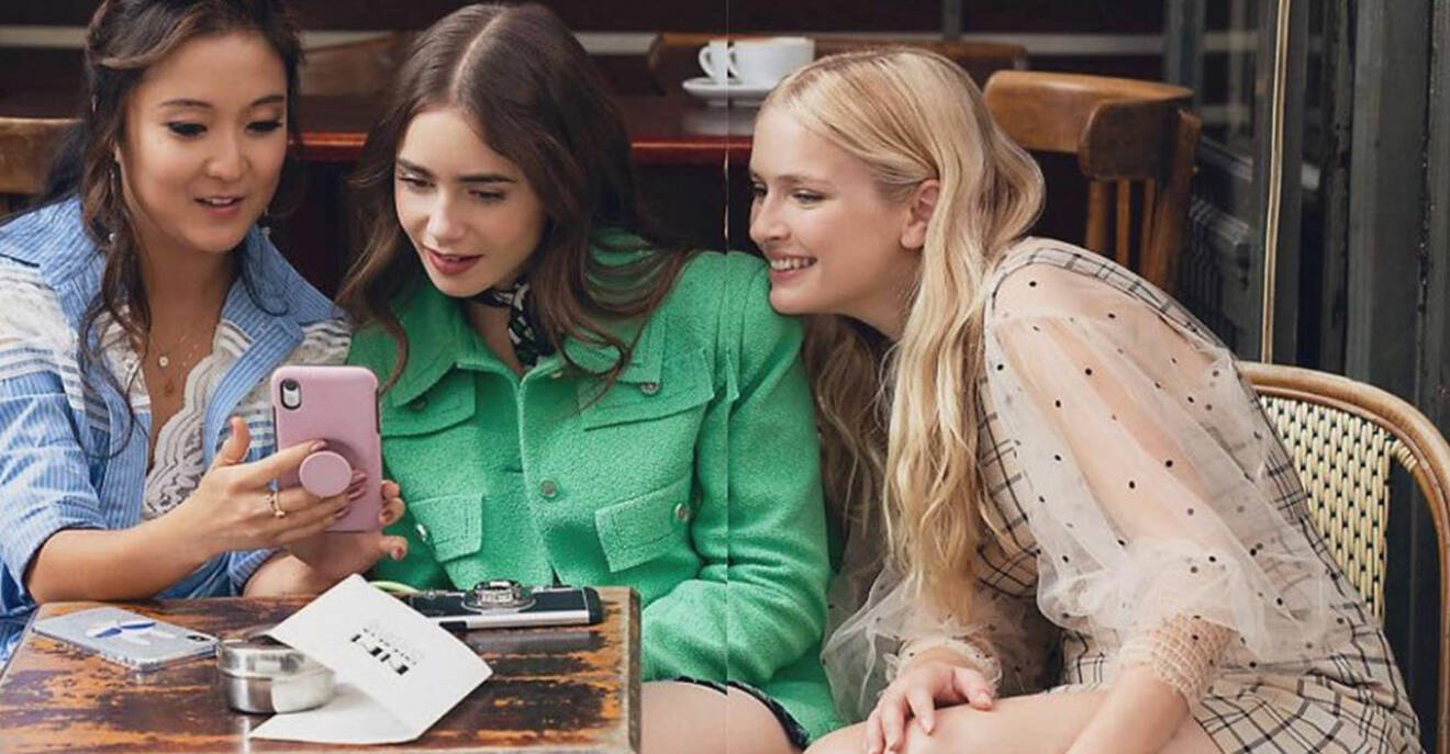 Emily in Paris och två vänner tittar på en mobiltelefon