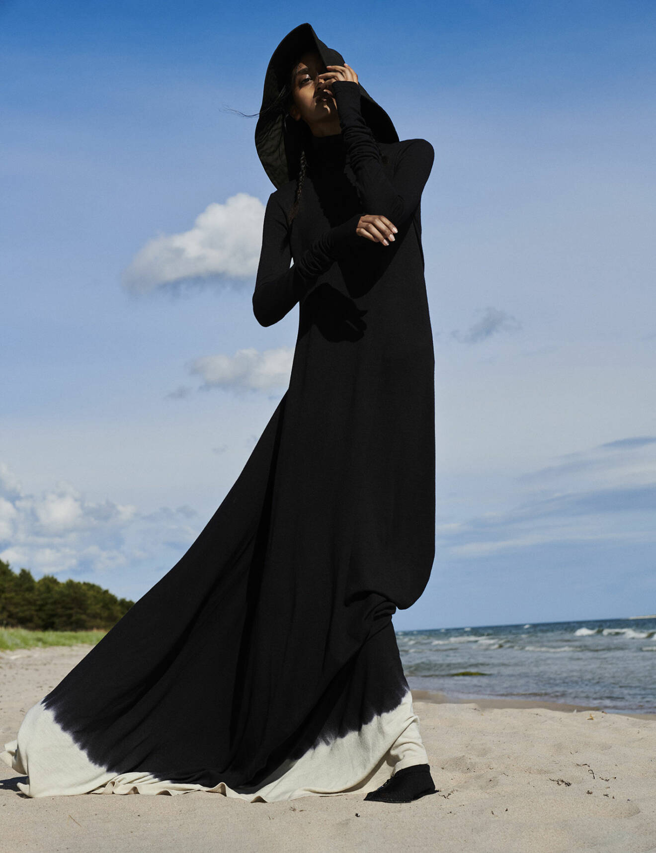 Modellen bär en svart klänning med vit detalj nertill och luva