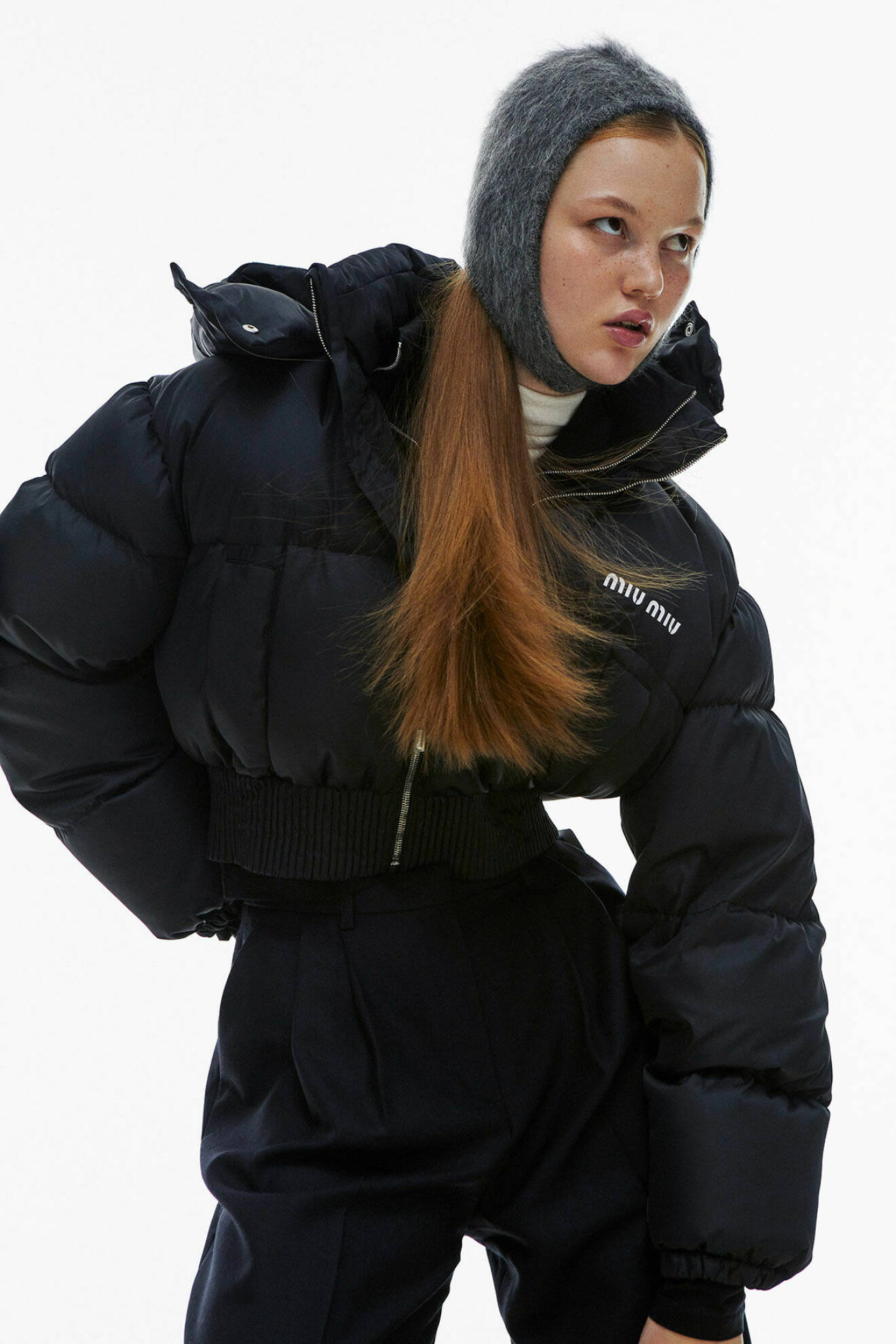 Modellen bär en svart, kort vinterjacka med en grå balaklava