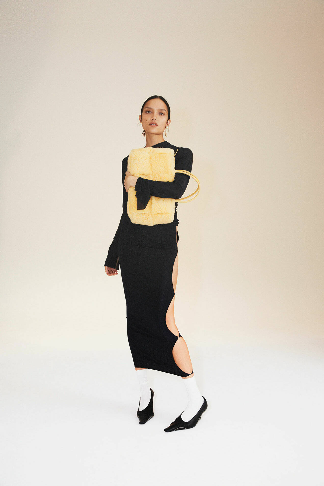 Modellen har på sig svart topp och svart kjol från Jade Cropper, hon bär på en gul väska från Bottega Veneta