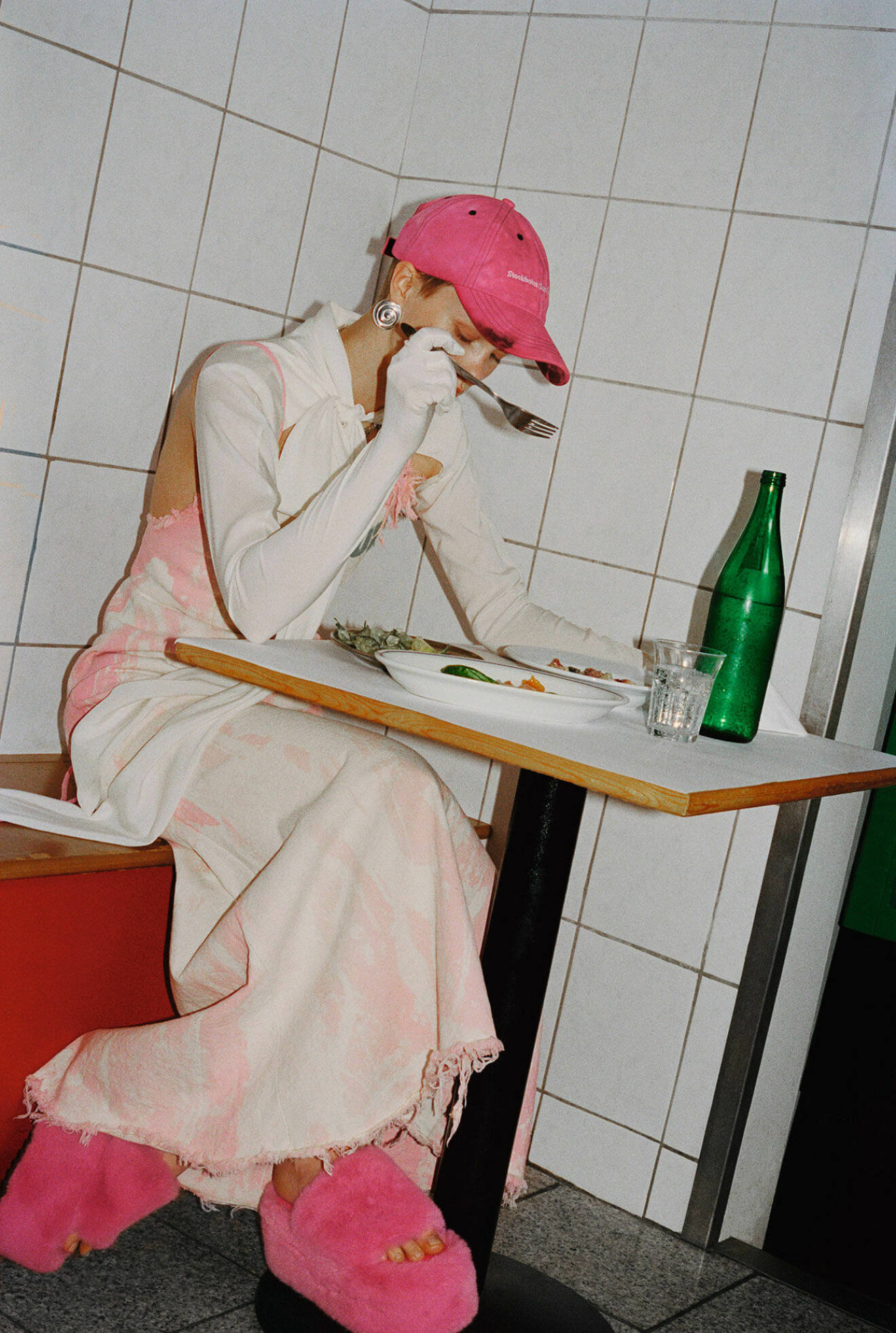 Modellen bär en lång klänning i vitt och rosa, vita handskar och en rosa keps