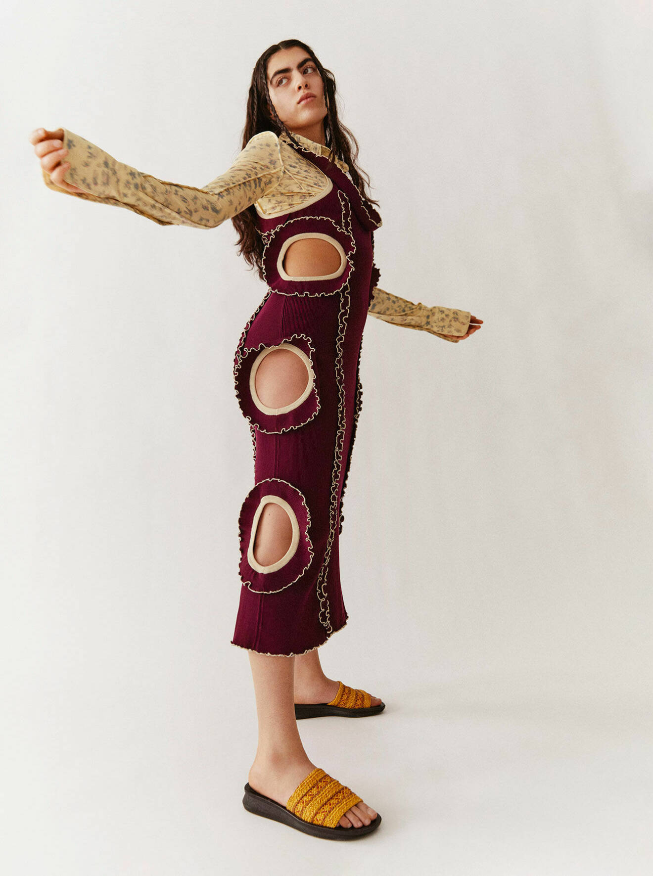 Modellen bär en vinröd klänning med cut out-detaljer och en blommig skjorta under