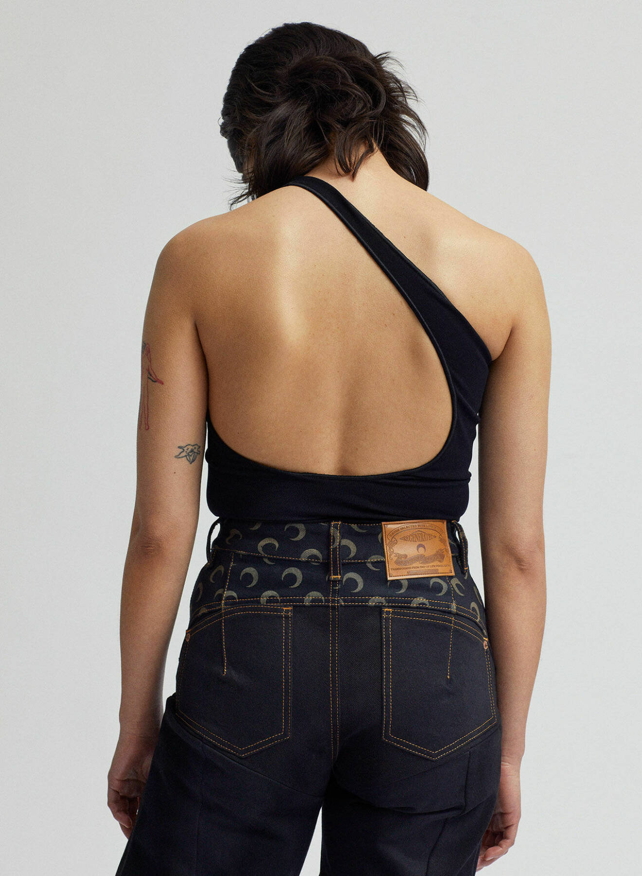 Modellen bär en topp med bar rygg av polyamid och elastan certifierat med Oekotex 100 tillsammans med upcyclade jeans