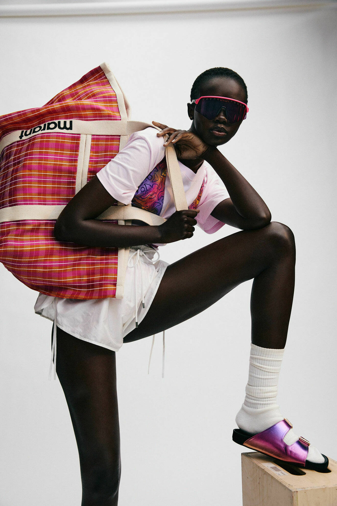 Fotomodellen bär en mönstrad bikinitopp, vita shorts och en stor rutig väska, allt från Isabel Marant