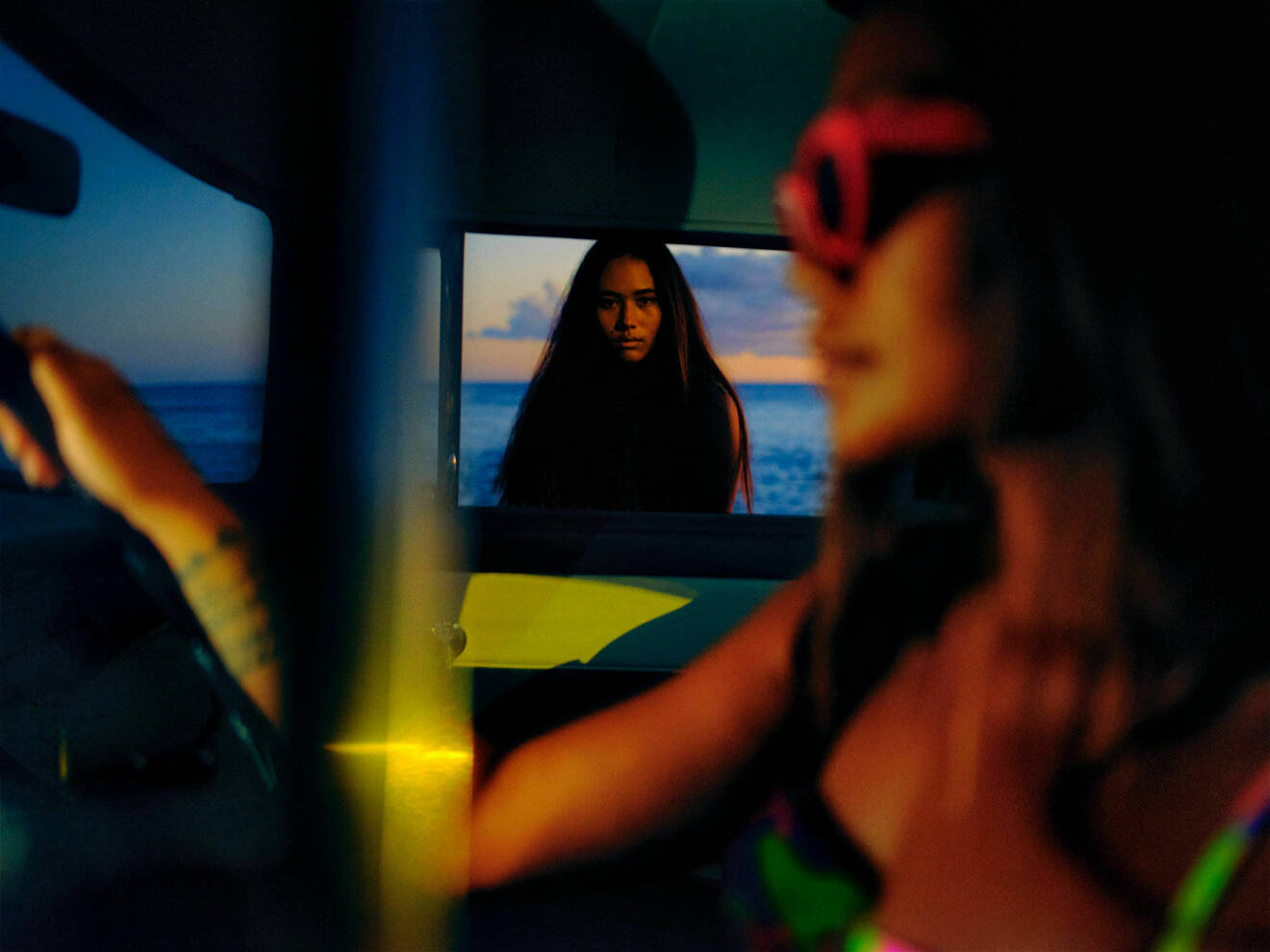 Fotomodellen sitter i en bil, hon har på sig röda solglasögon och en bikinitopp