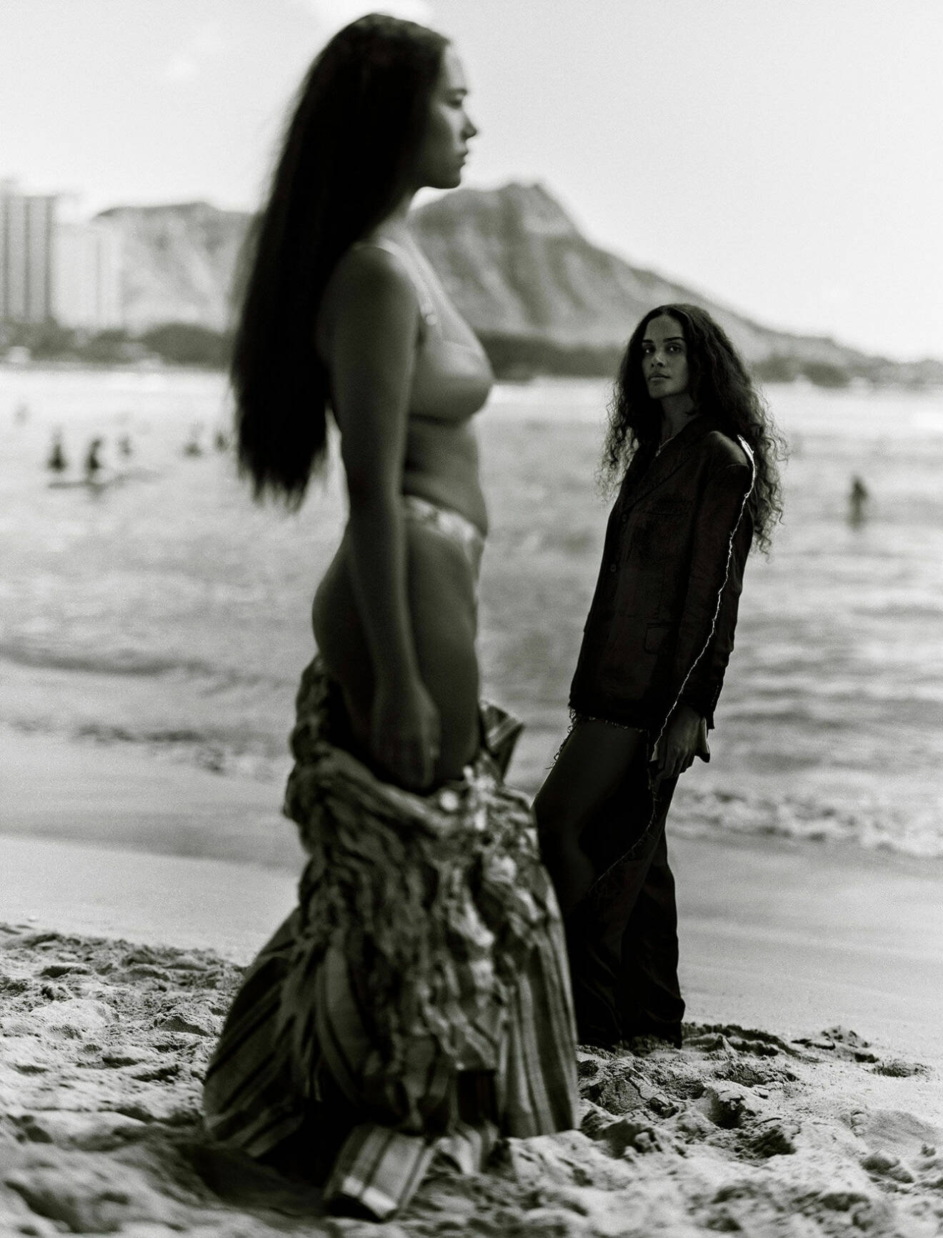 Naya har på sig bikini och rutig jacka. Aloha bär kavaj och kjol. Båda står på stranden.