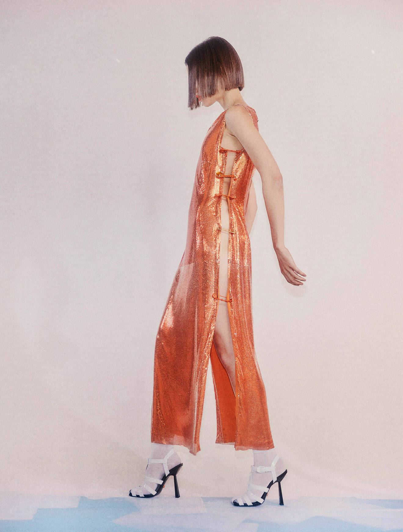 Fotomodellen har på sig en lång skimrande klänning i orange med cut out-detaljer