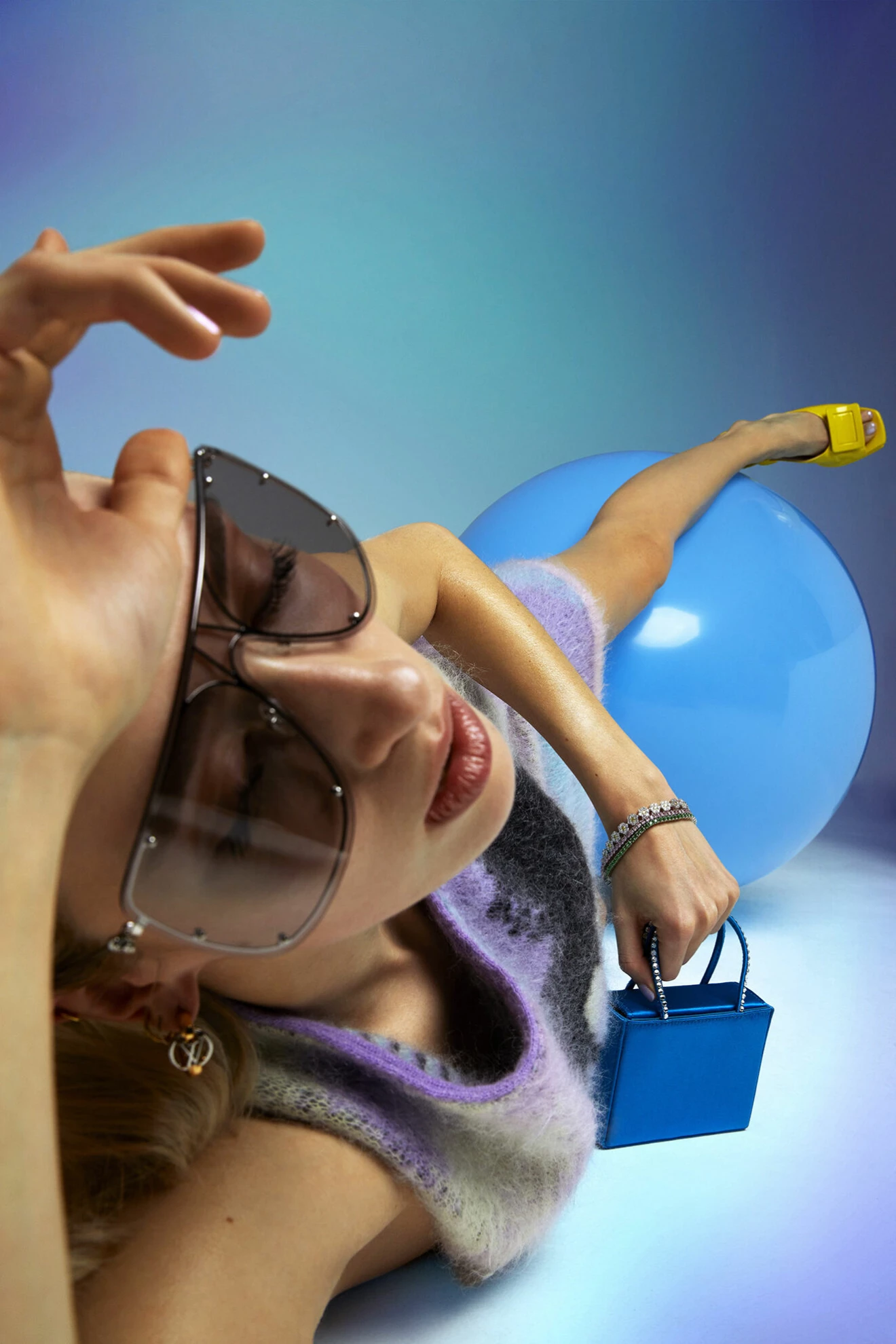 Fotomodellen har på sig en lila klänning med mönster från Loewe och en miniväska i blått från Amina Muaddi