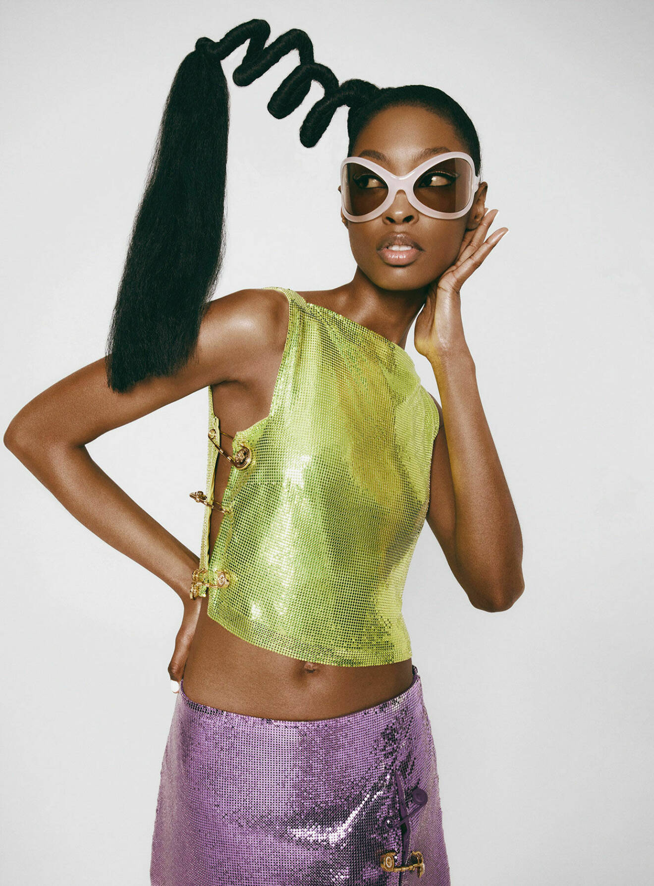 Modellen bär en skimrande grön topp med en skimrande lila kjol, båda plaggen från Versace