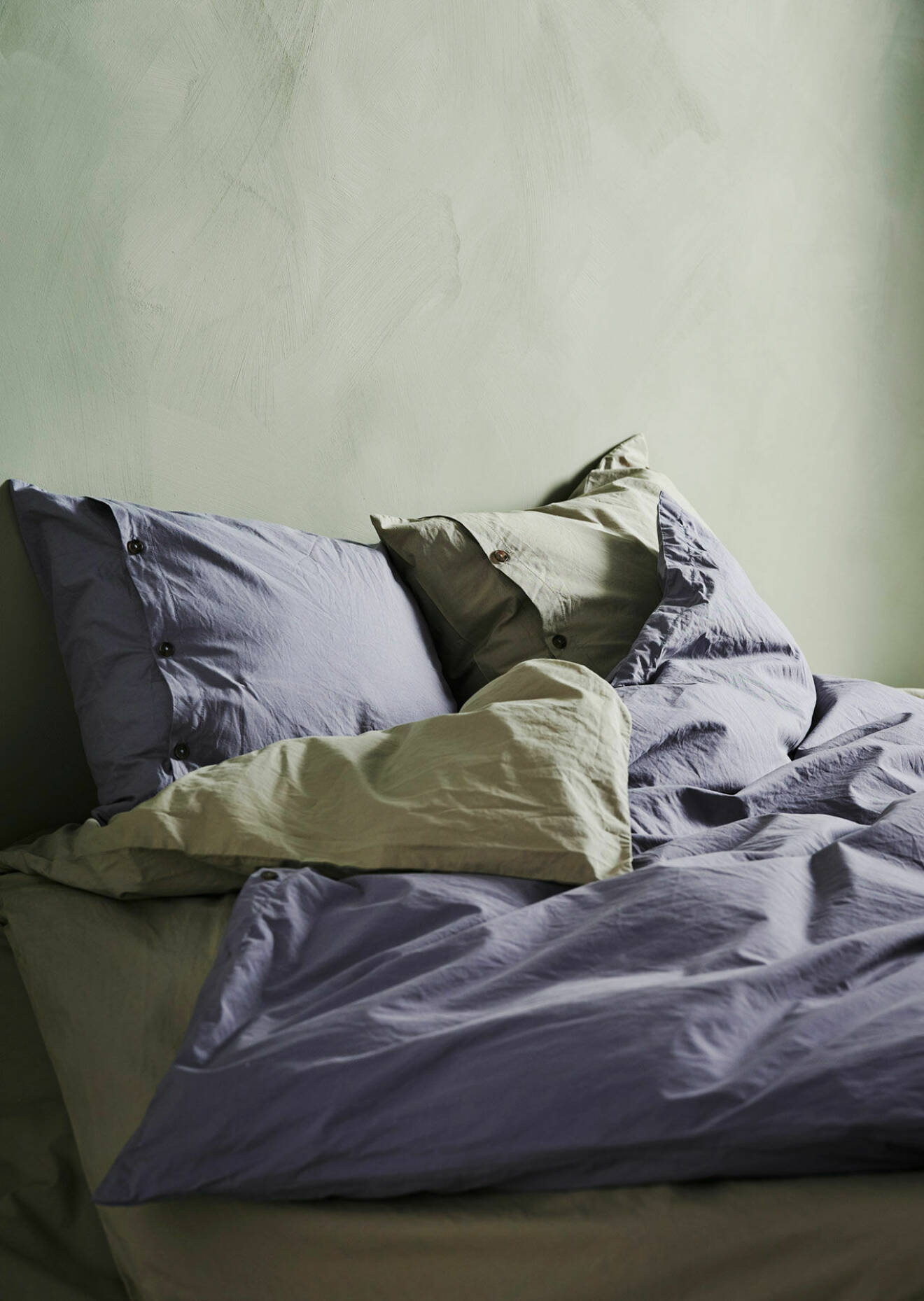 Sängkläder i en ljusare lila och beige färg med knappdetaljer.
