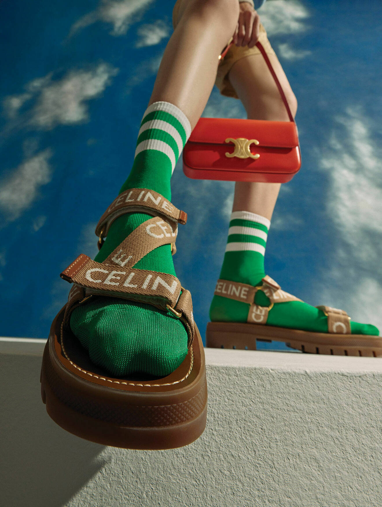 Modellen har på sig bruna sandaler och en håller i en röd handväska, båda från Celine by Hedi Slimane