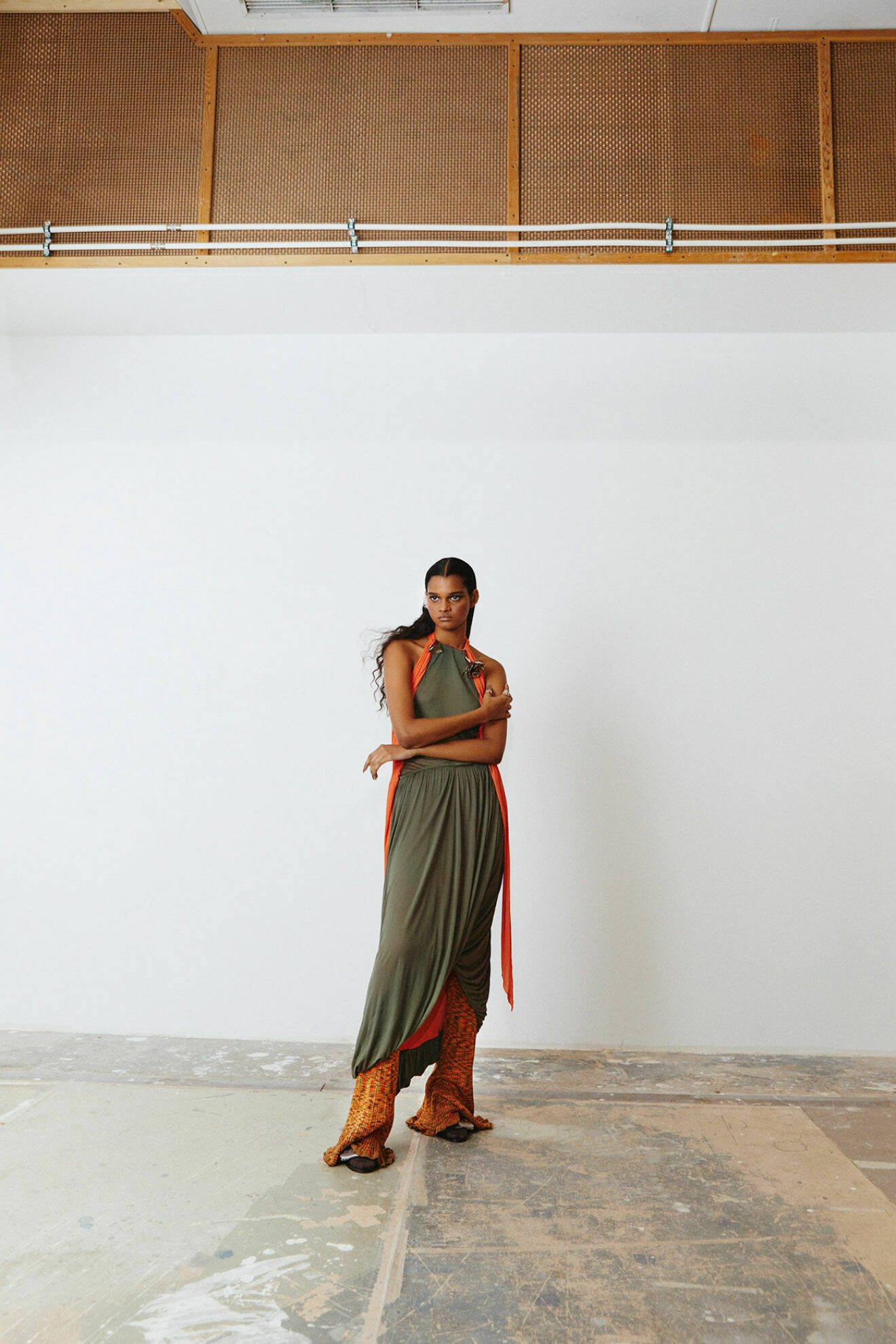 Fotomodellen har på sig en grön klänning med orange detaljer, från Loewe med mönstrade byxor, från Acne Studios.