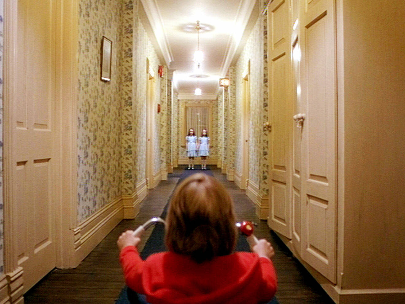 Den femåriga Danny sitter på en trehjuling i förgrunden när han ser tvillingspökena vid korridorens slut.
