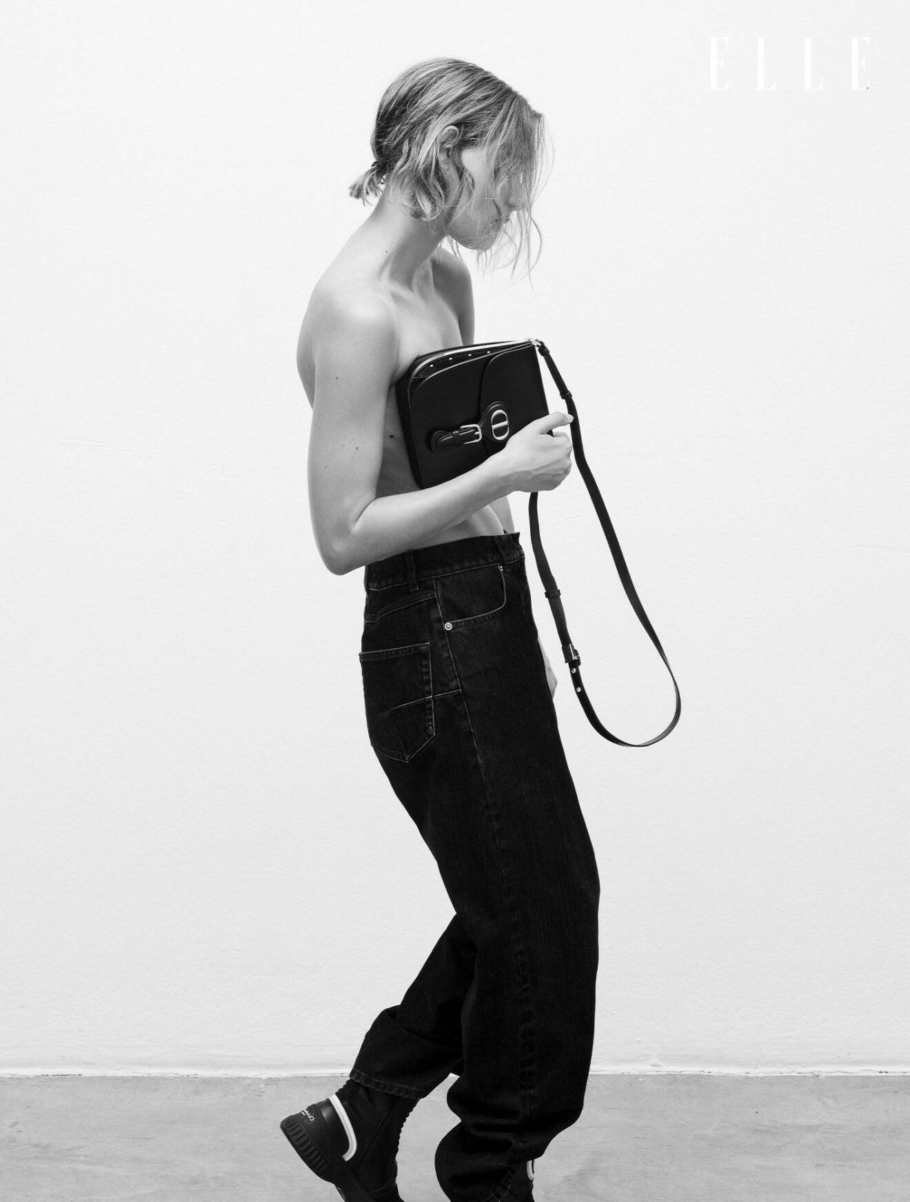 Fotomodellen har på sig svarta jeans och en bär en svart handväska, båda från Dior.