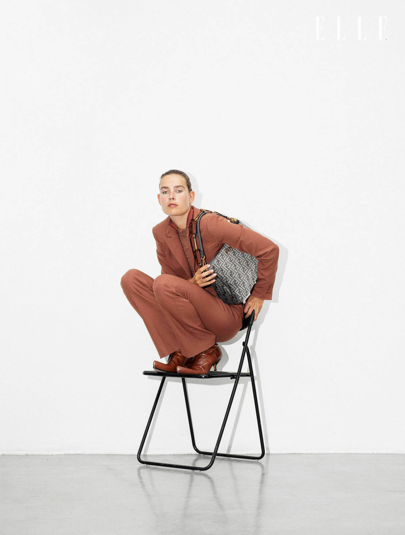 Modellen sitter på huk på en stol och hon har på sig en brun kavaj med matchande byxor till, allt från Fendi.
