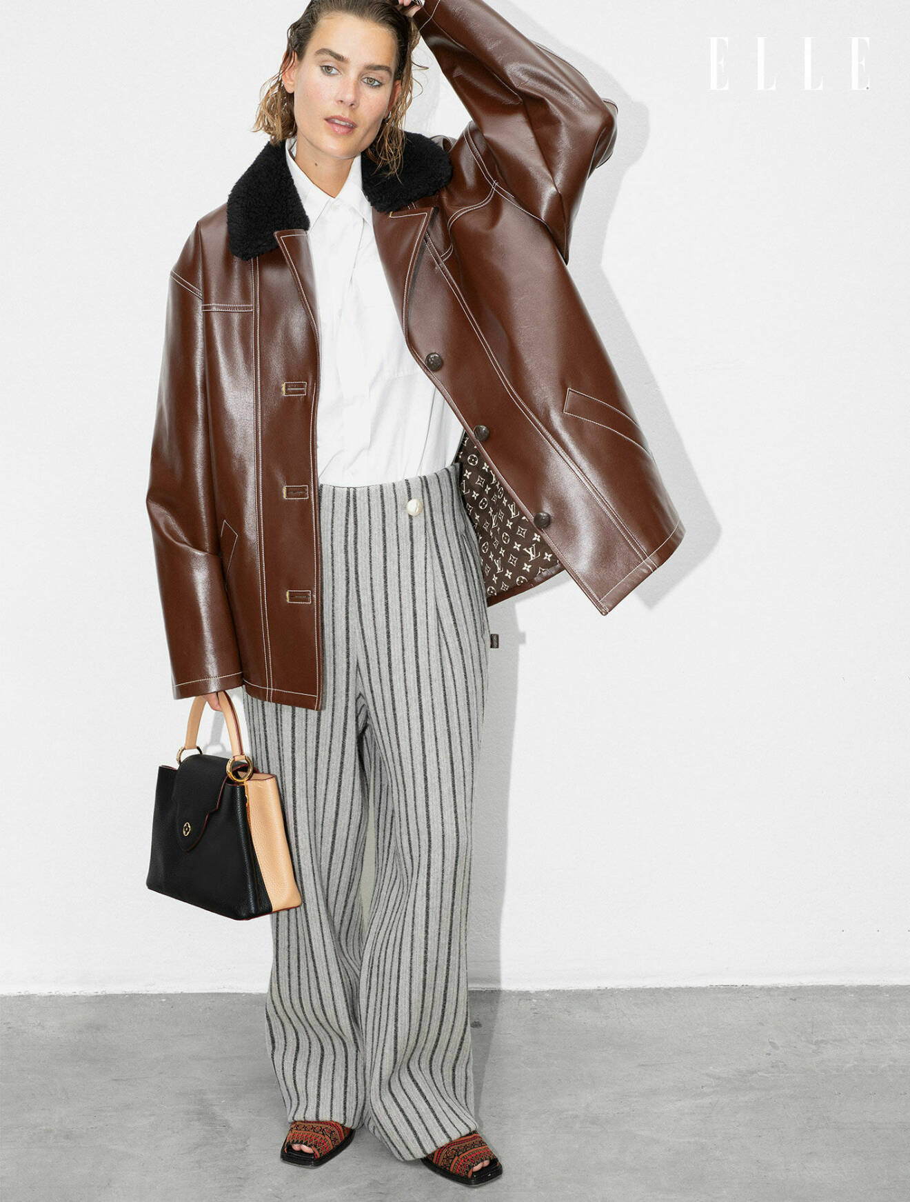Modellen bär en brun jacka, vit skjorta och randiga byxor, allt från Louis Vuitton.