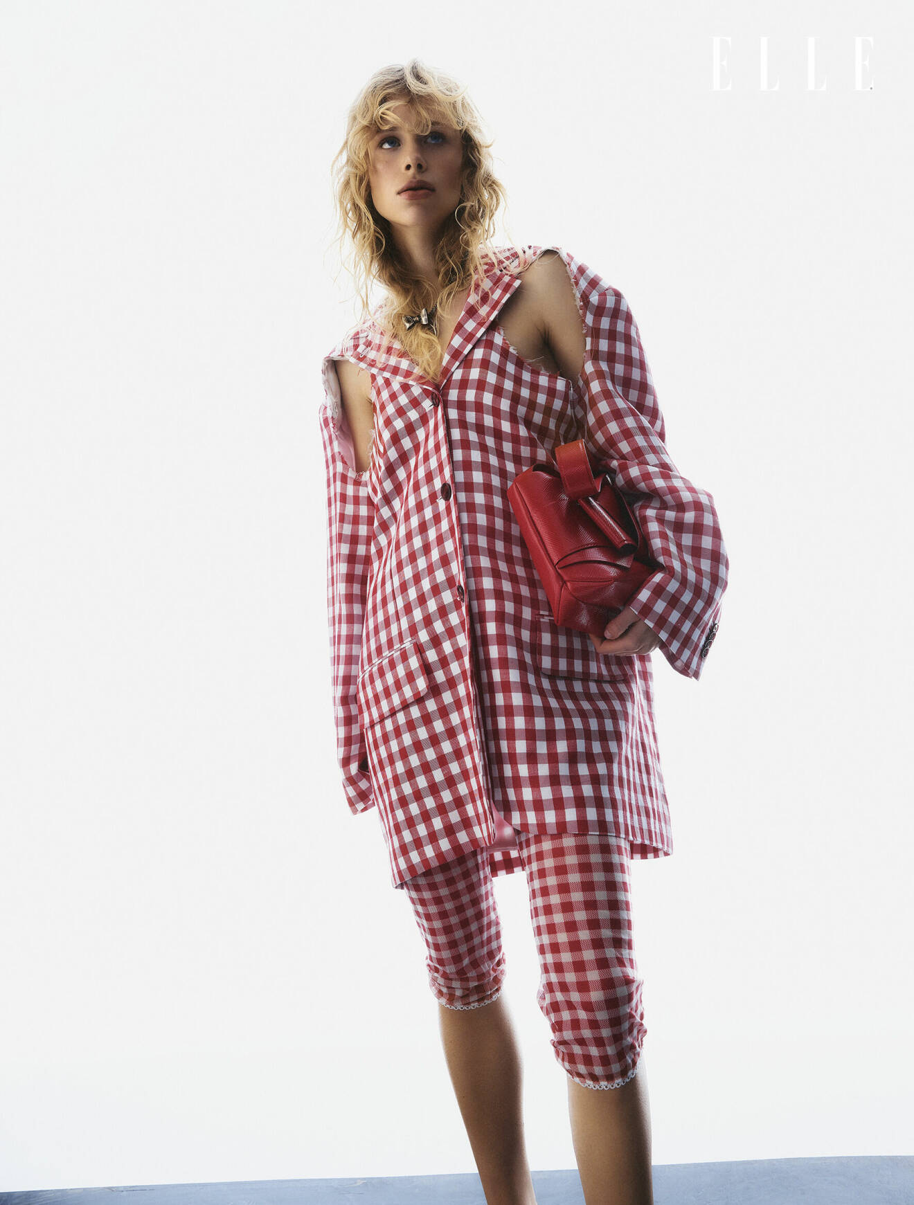 Modellen bär en röd- och vitrutig kavaj med matchande byxor tillsammans med en röd väska, allt från Acne Studios