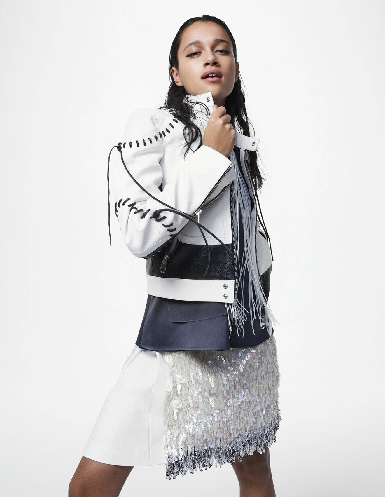 Modellen bär en vit jacka med svarta detaljer från Chloé, tillsammans med topp och en kjol med paljetter, båda från Jil Sander by Lucie and Luke Meier