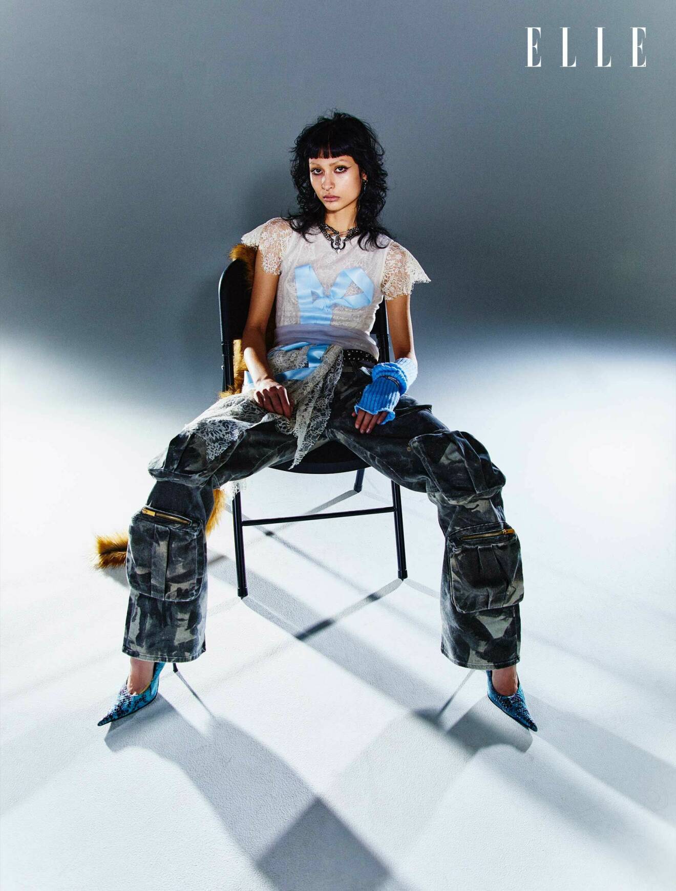 Fotomodellen sitter på en stol, hon har på sig en t-shirt med spetsdetaljer, byxor och mönstrade pumps.