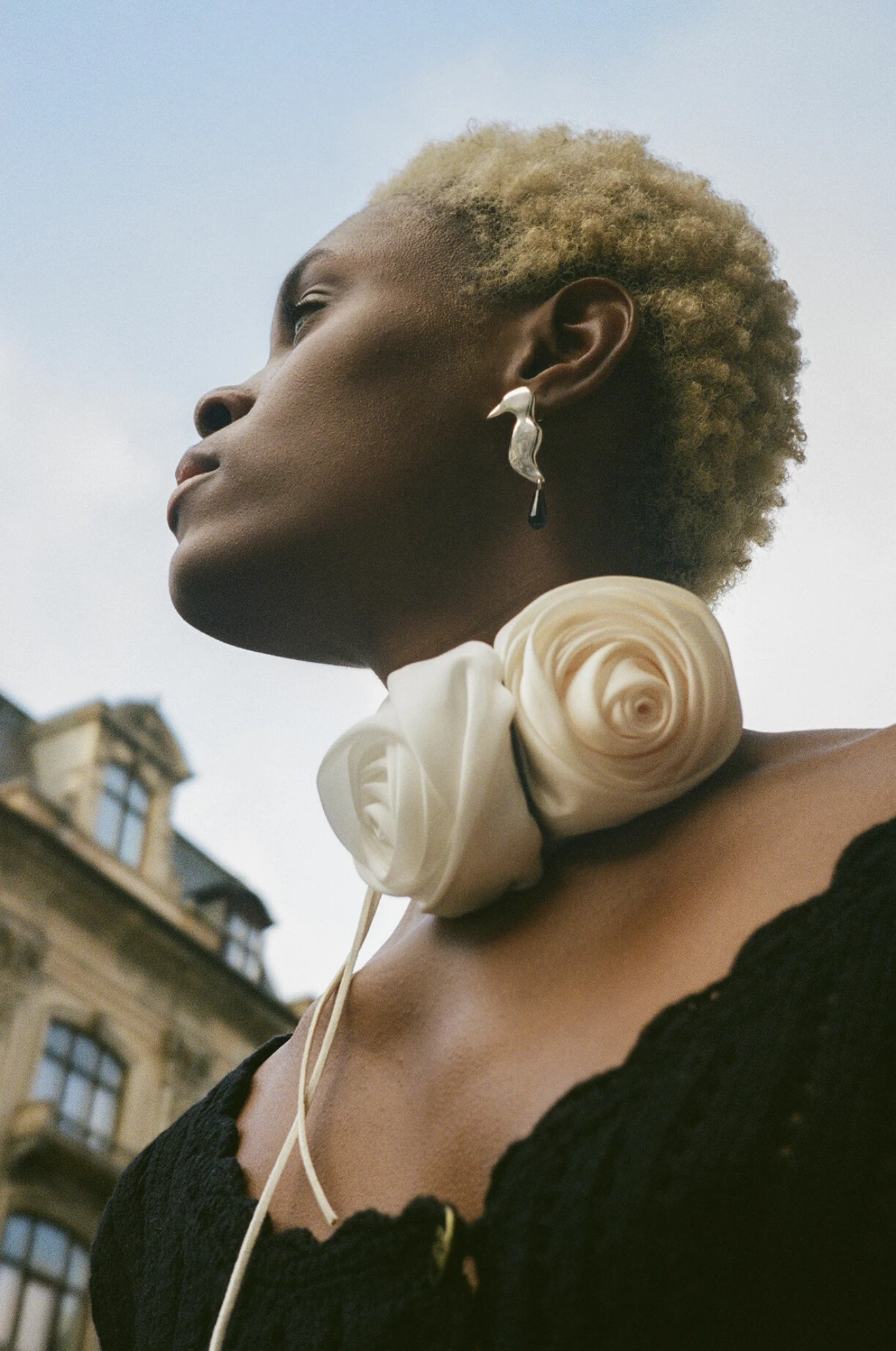 Modellen bär en svart kofta och ett halsband med två stora vita rosor i siden.