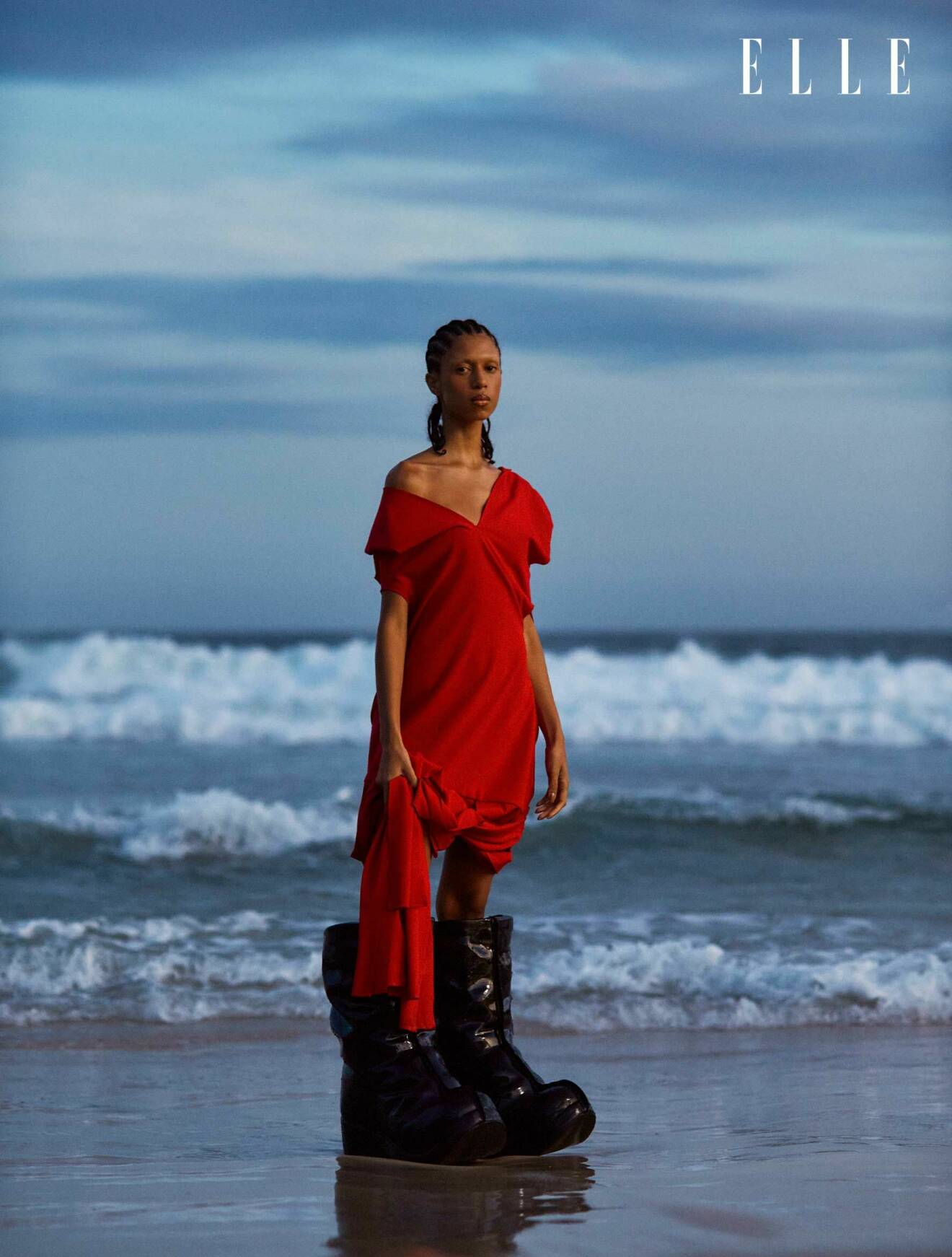 Fotomodellen står framför havet, klädd i en röd klänning från ROcio Canvas