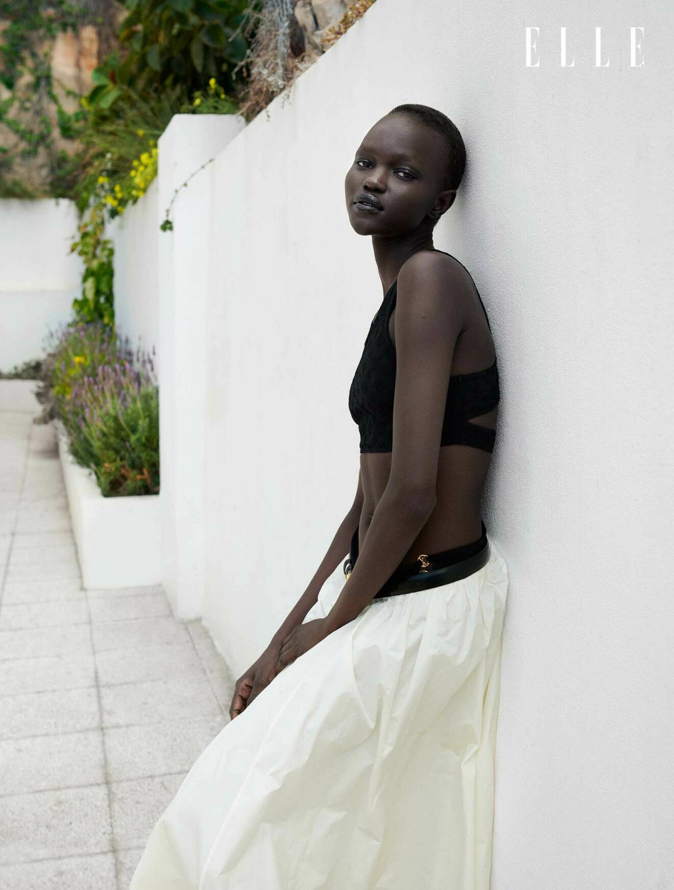 Modellen står lutad mot en vägg, hon har på sig en svart bikini från Louis Vuitton och en lång vit kjol från House of Dagmar