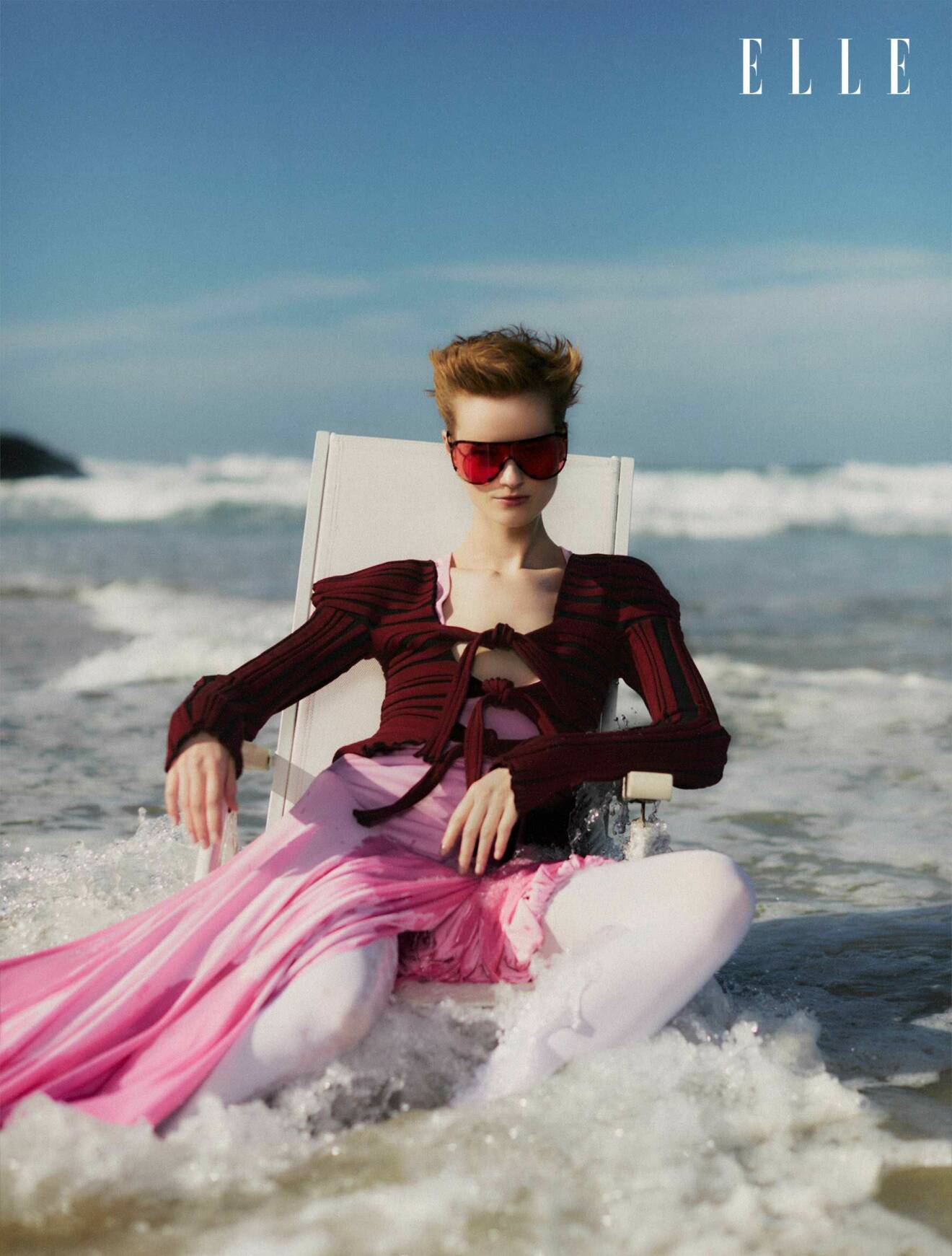 Modellen sitter i en stol i havet, hon har på sig en rosa klänning från Christopher Esber och en långärmad tröja från Katharina Dubbick