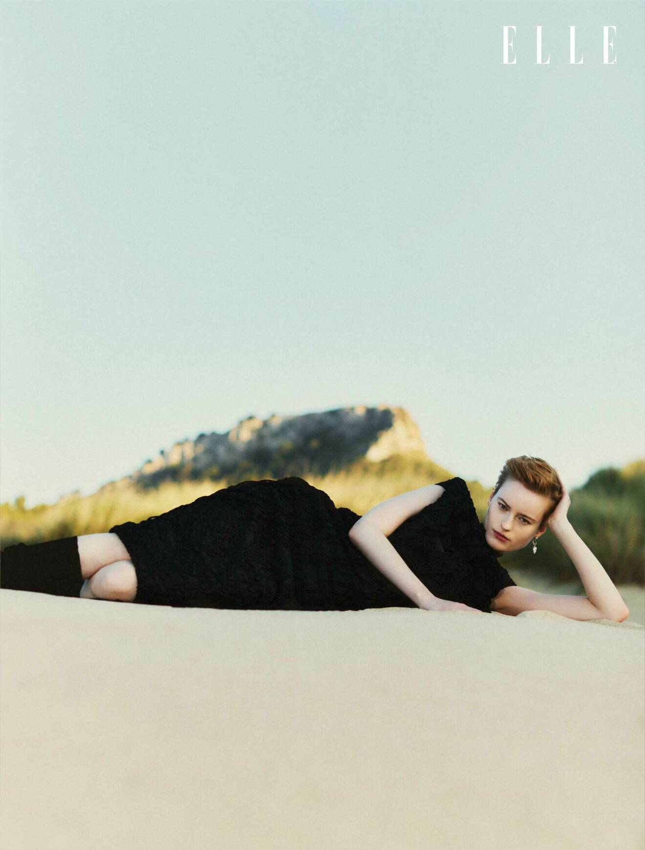 Modellen ligger ner i sanden och har på sig en svart klänning från Dries Van Noten och svarta benvärmare från Katharina Dubbick.