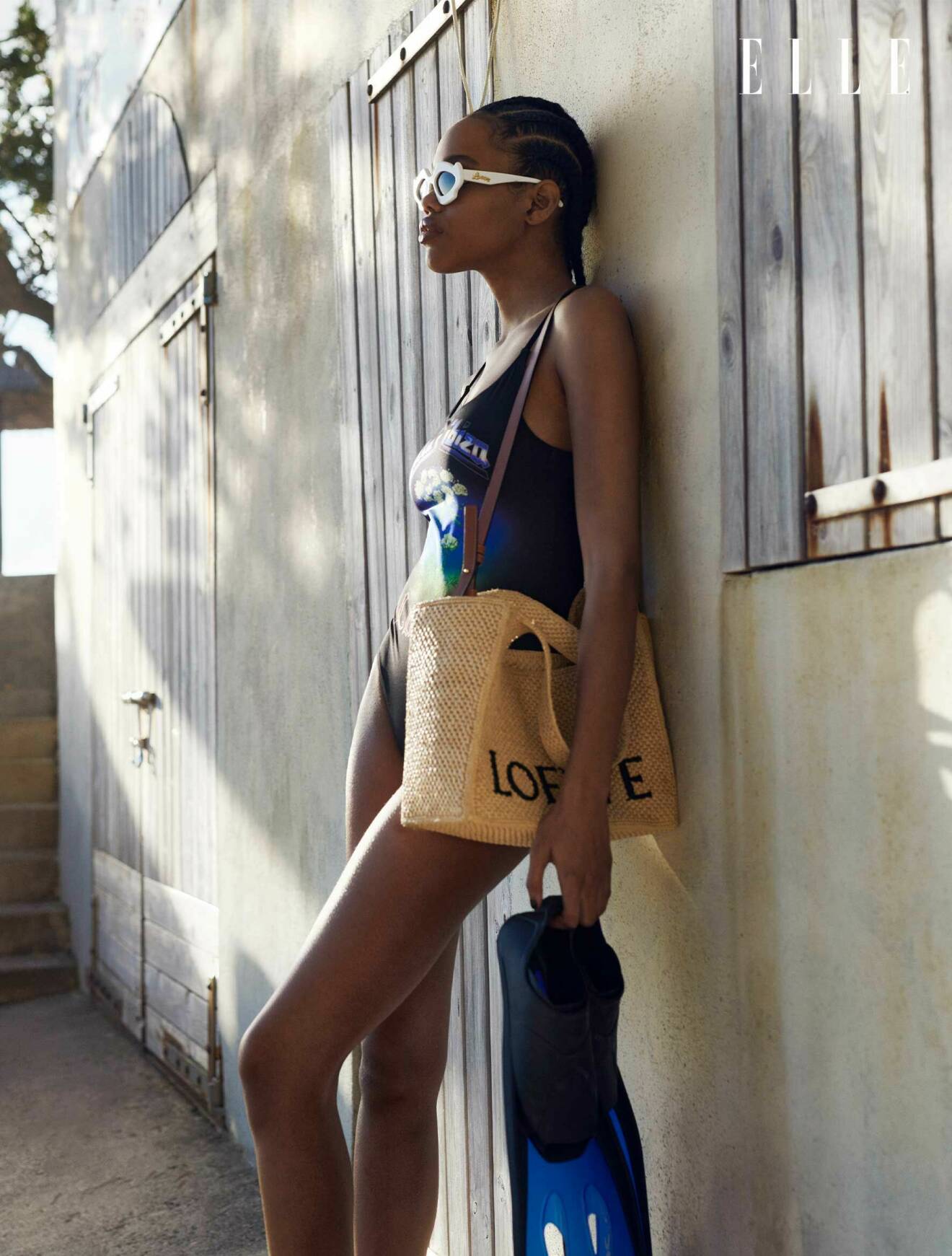 Fotomodellen står lutad mot en vägg, hon har på sig en mönstrad baddräkt, solglasögon och en strandväska, allt från Loewe