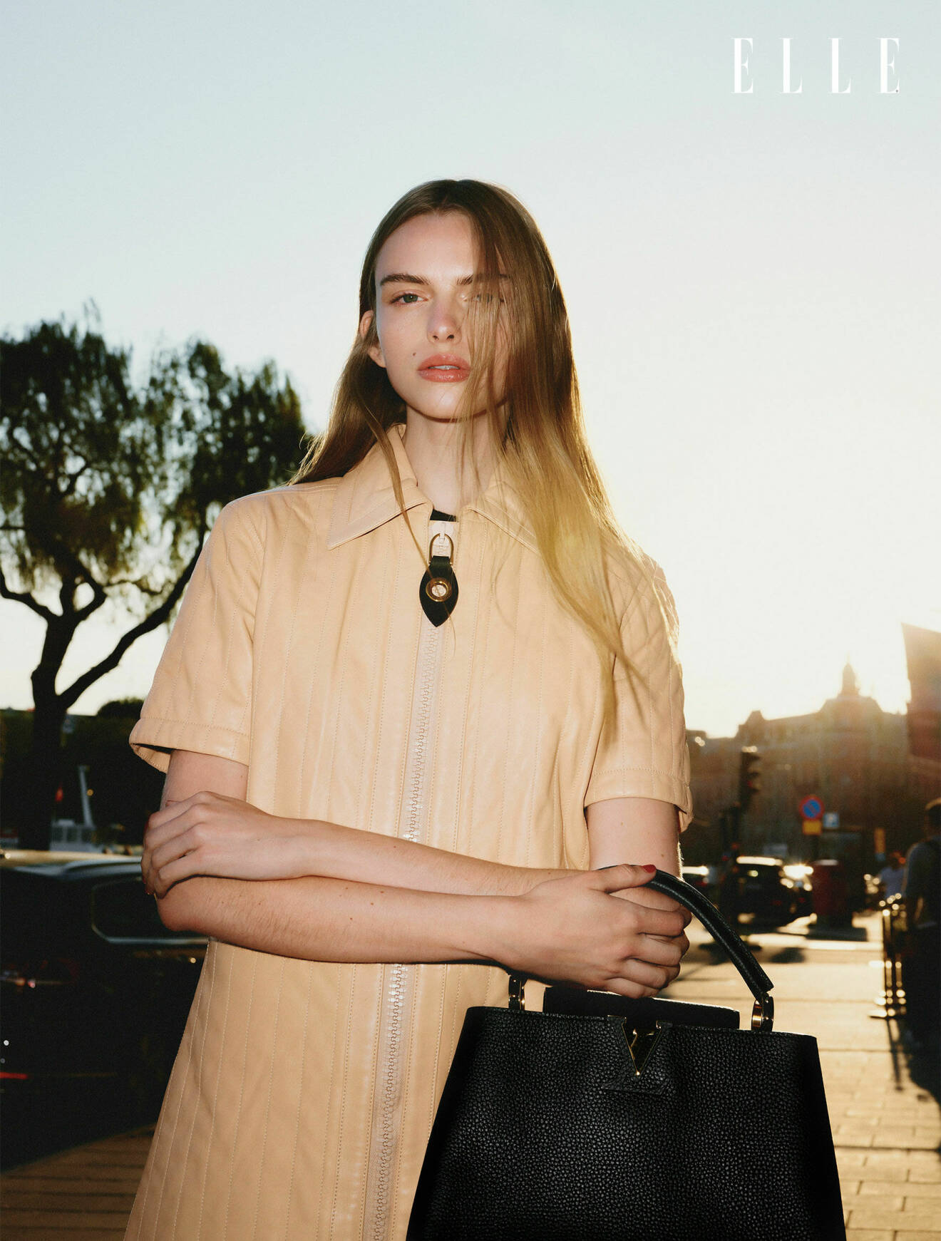Fotomodellen har på sig en beige klänning och har en svart väska på armen, båda från Louis Vuitton.