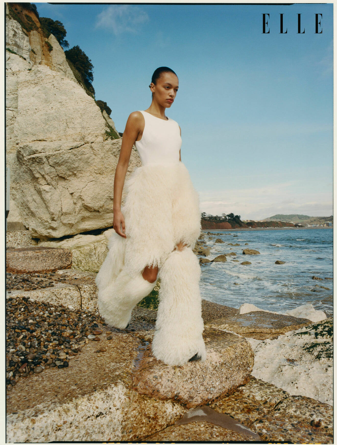 Modellen bär en vit klänning med lurvig kjol tillsammans med lurviga benvärmare, allt från David Koma.