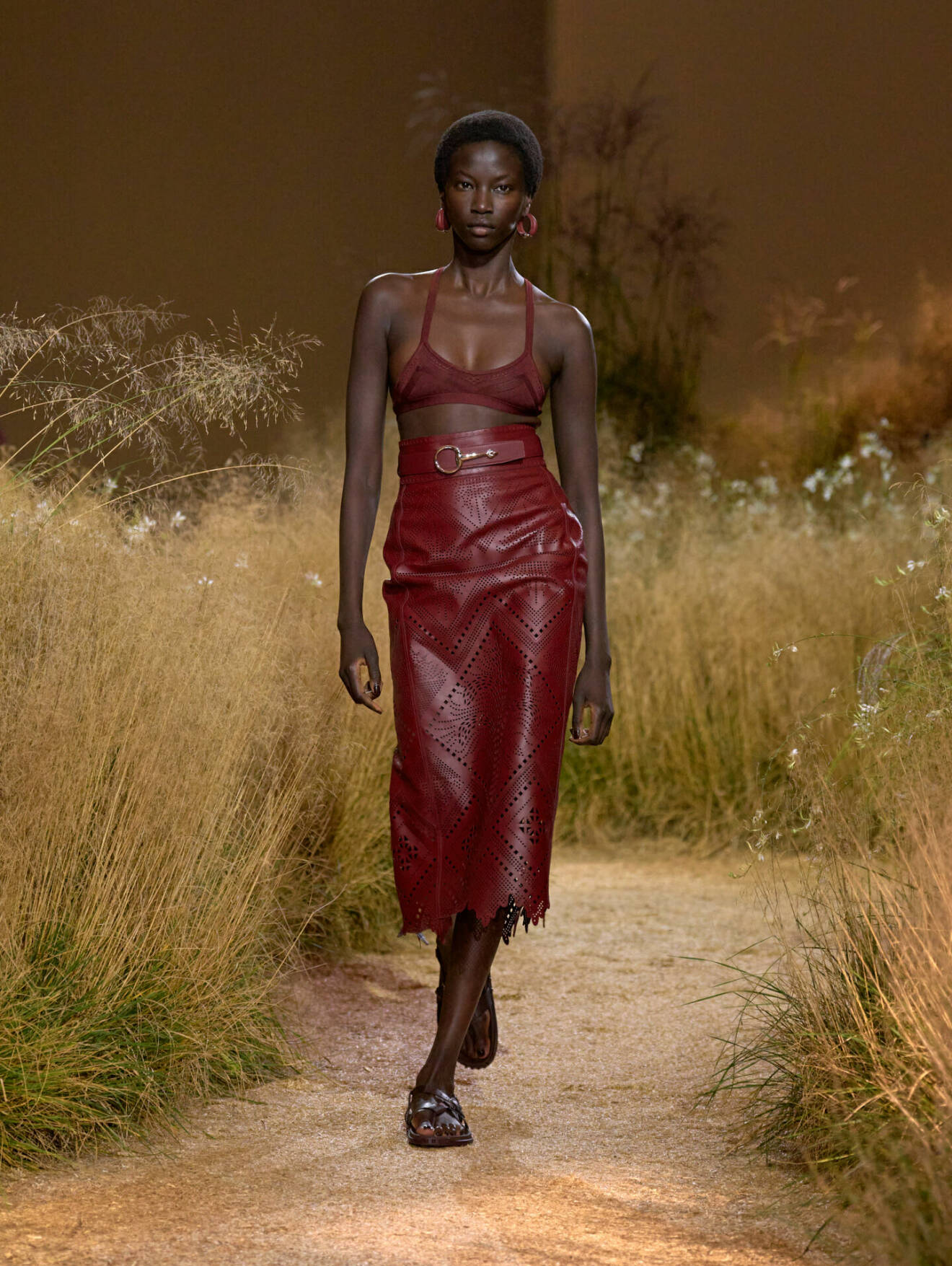 Röd look med behå-topp och läderkjol från Hermès SS24 visning. 
