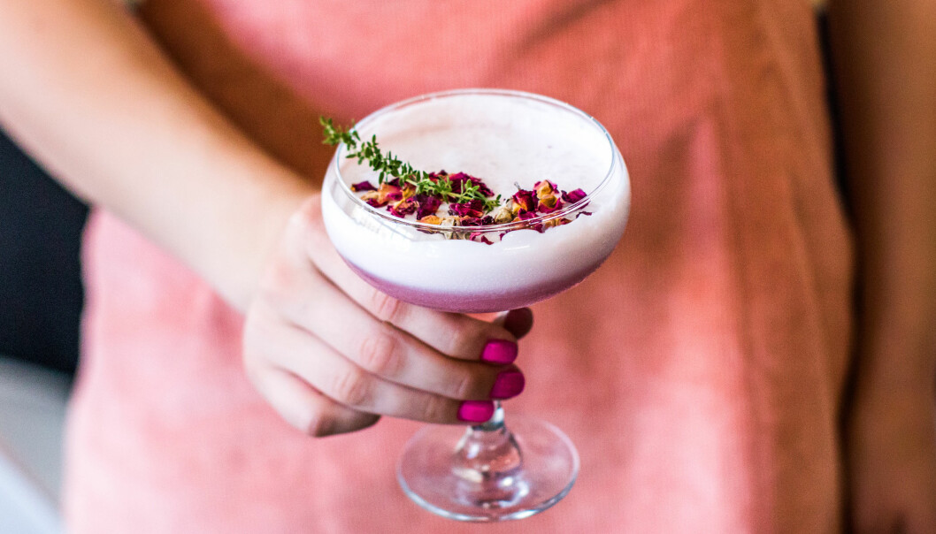 kvinna håller i lila drink med skum och blommor