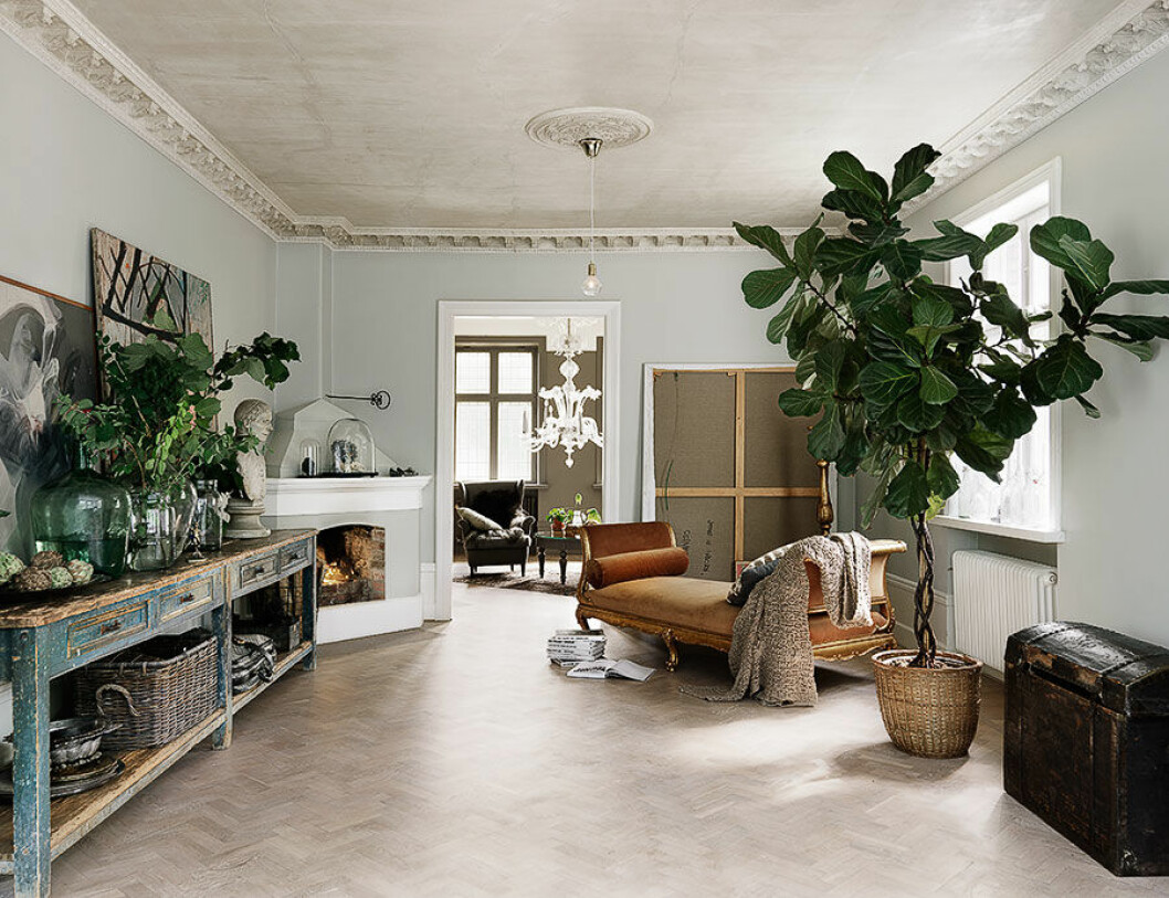 <strong>Foto::</strong> <a href="http://www.petrabindel.com/" target="_blank" rel="noopener">Petra Bindel</a> Bilden publicerades ursprungligen i hemma hos-reportaget <a href="https://www.elle.se/decoration/kika-in-i-var-bloggare-malin-perssons-ljuvliga-hem/">”Kika in i vår blgogare Malin Perssons ljuvliga hem!”</a> Damianos gammelfarfars byst vakar över vardagsrummet. ”Barnen brukar säga att hans ande bor där”, säger Malin. Den vackert patinerade arbetsbänken räddades från soptippen i en antikbutik i Rom – det enda Malin behövde göra var att renovera lådorna invändigt. Taket, med både sprickor och missfärgningar, lämnades som det var. ”Det blev en härlig, dekadent känsla.” Schäslongen är inköpt på auktion i Italien. Även 1800-talskistan kommer från Rom. Den stora tavlan är målad av Martin Bradley. Glas och keramik, loppisfynd. Lampa Diamond Lights, design Eric Therner, Frama.