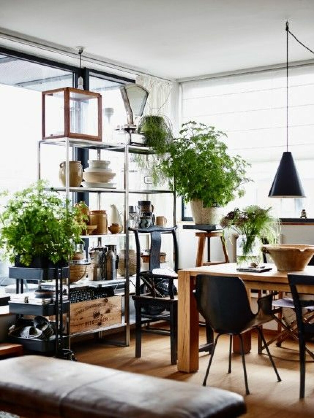 Framför de stora fönstret ut mot altanen står rostfria hyllor designade av Jon Karlsson för Ikea, som låter ljuset strila in på matplatsen. Här står moccabryggare och vackra lergodsföremål samlade. Den gamla apoteksvågen är köpt på Bukowskis Market. matplats-växter-snygg-hylla-förvaring foto andrea papini