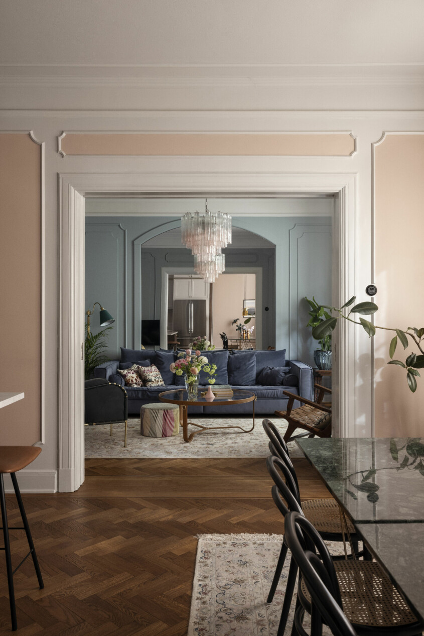 Blick från kök mot vardagsrum. Det breda dörrpartiet rymmer dubbla skjutdörrar. Spegeln bakom soffan från Room skapar djup och delar av köket reflekteras i den. Muranolampan är hemmets center piece. Dess mjukt rosa färg tas upp i de nya listverken på väggarna. Nazli Zias hem
