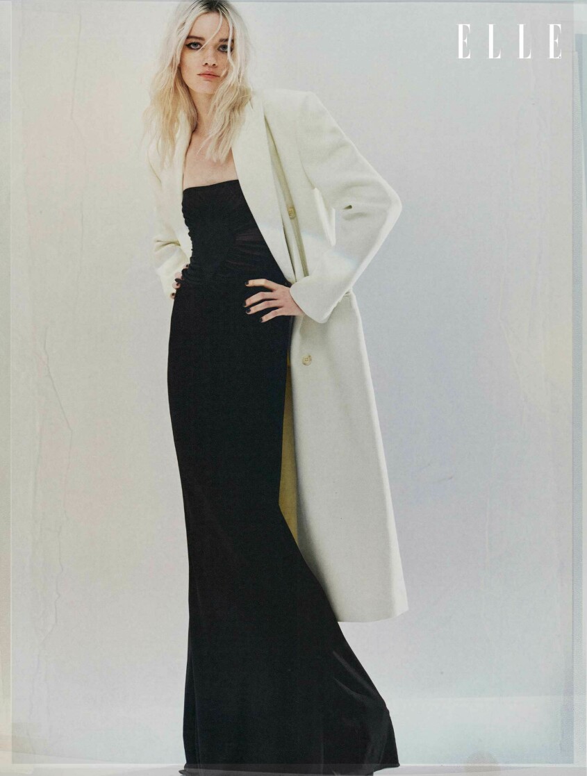 Modellen bär en lång vit kappa från MM6 Maison Margiela över en svart topp och kjol från Saint Laurent.