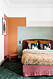 Färgglatt sovrum med orange-grön vägg och färgglada textilier på sängen