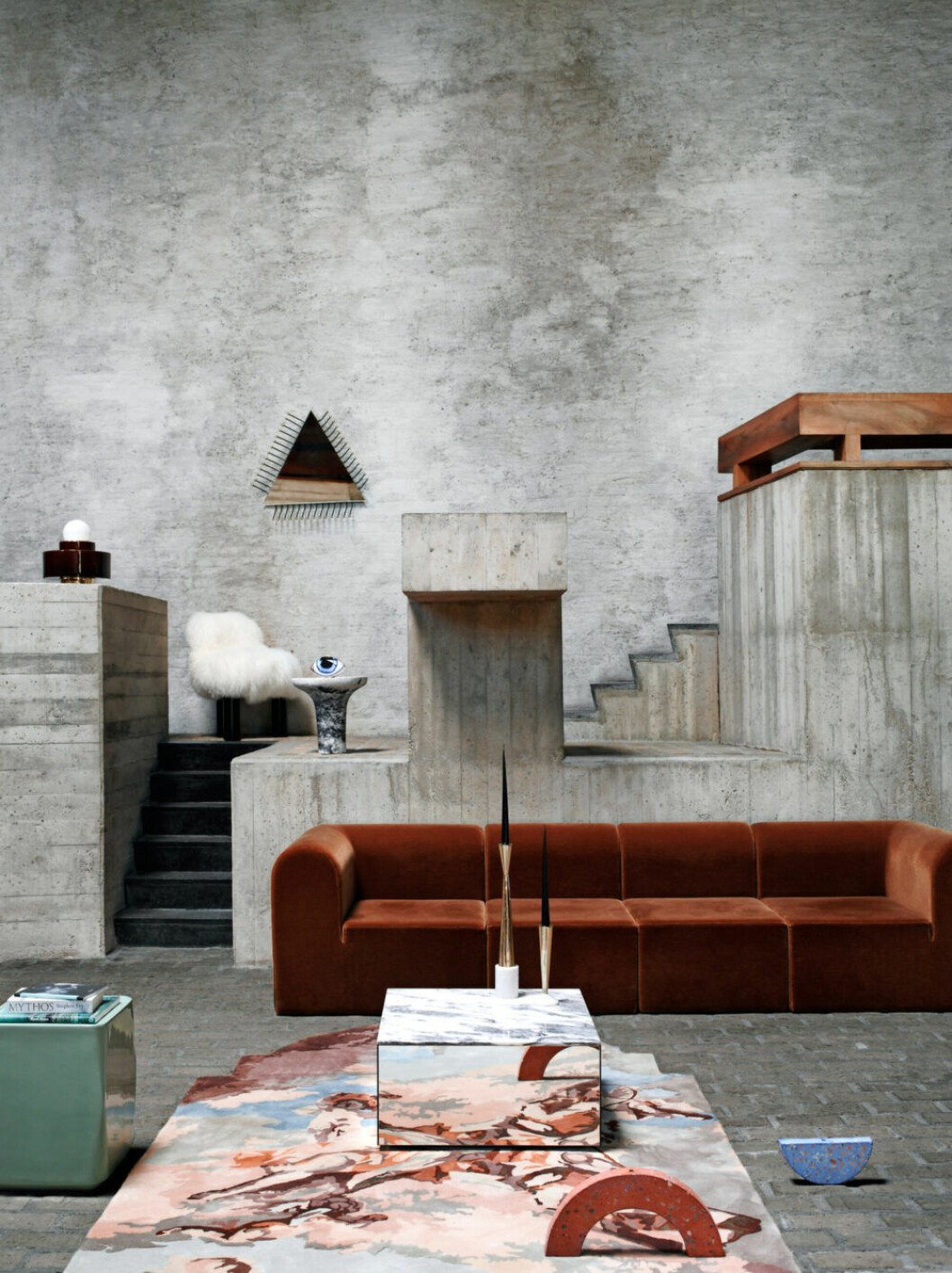 Litet sidobord av keramik, Christophe Delcourt/Co van der Horst. Lampa <em>Table Light 1.04</em>, Haos. Matta <em>Commialo Di Venere</em> av Alessandra Baldereschi, Nodus. Stol <em>Botolo</em> av Cini Boeri, Arflex. Spegel <em>Motherboard</em> av David/Nicolas, Collection Particulière/Co van der Horst. Litet bord och brevpress i form av öga, L’Objet/Zomers Bloemen. Modulsoffa av Erik Rasmussen, Paustian. Soffbord <em>Mirror</em>, Kristina Dam. Ljusstakar ur kollektionen <em>Stone</em>, Tom Dixon. Handstöpta ljus, Ester & Erik. Blå och rosa skulpturer, Studio Thinkinghand. Rostbrun modulsoffa från Paustian tillsammans med grafiskt mönstrad matta i ett grått rum
