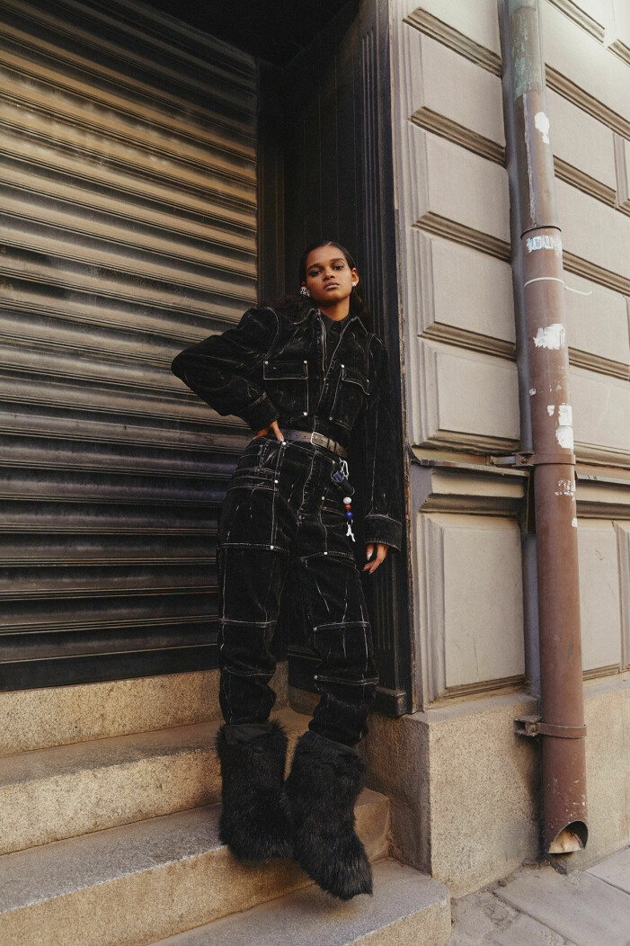 Jumpsuit, 14 975 kr, Stella McCartney. Skjorta, 3 500 kr, Blank Atelier. Bälte, 2 840 kr, och airpodfodral, 1 980 kr, båda Saks Potts. Nyckelring, 860 kr, Kerne Milk. Boots, pris vid beställning, Stand Studio. Örhängen, 3 800 kr, Arto. Modellen bär en svart jumpsuit från Stella McCartney, skjorta från Blank Atelier och boots från Stand Studio.
