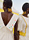 Två kvinnor i flätstilen cornsrows med pärlor längs flätornas slut. Klädda i krämvita klänningar med olika broderade motiv, från Sindiso Khumalo x &amp; Other Stories designssamarbete