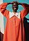 Kvinna med stort leedende och bär på en rödorange lång klänning med vitkrage från Sindiso Khumalo x &amp; Other Stories designsamarbete