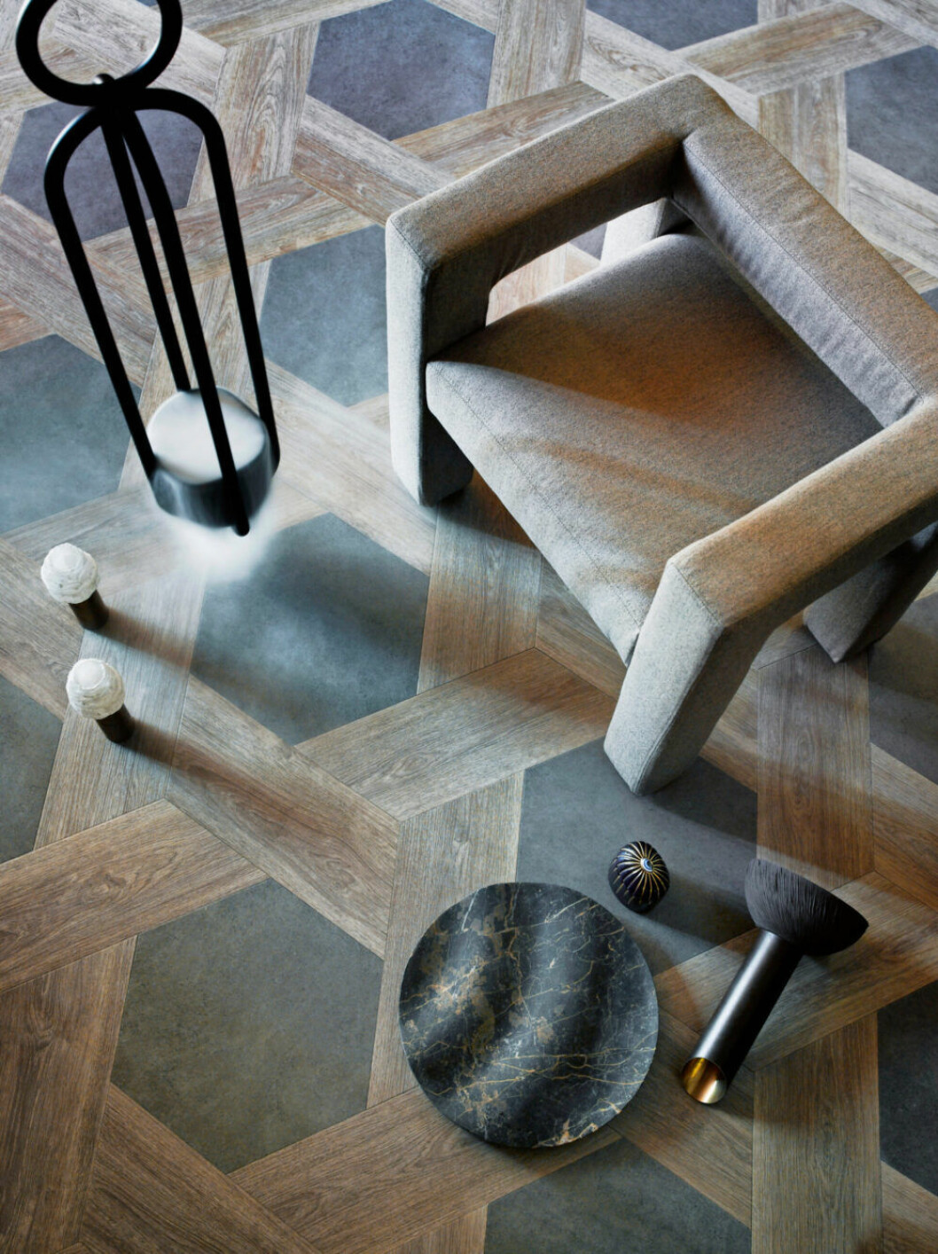 Ljusstakar av Sophia Dries. Vinylgolv <em>Big Hexagon Jura Stone</em> och <em>Verdon Oak</em>, Moduleo. Ampel för växter, Atelier Haussman/Edha Interieur. Fåtölj <em>Toptun</em>, Faina Design. Fruktskål <em>Ripple</em> av Dan Yeffet, Collection Particulière/co van der Horst. Vas <em>#1B</em>, Sophie Dries. Objekt <em>Lito Candle</em>, L’Objet/Zomers Bloemen. Små inredningsdetaljer som ljusstakar och fruktskål tillsammans med fåtölj, allt i ljusgråa toner på ett ljusbrunt golv